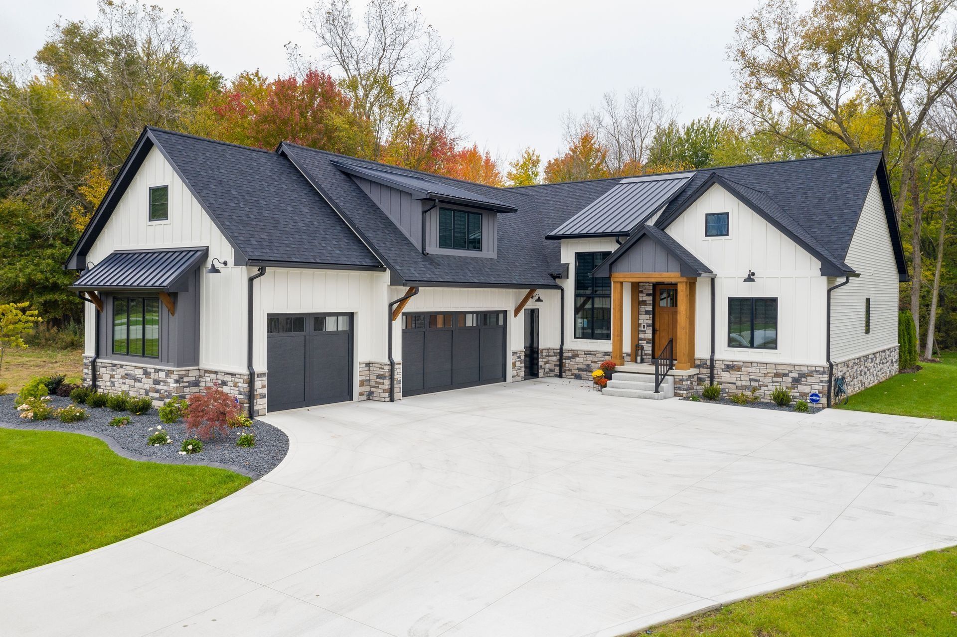 Modern white house with dark gray roof and garage doors, stone accents, and a concrete driveway.