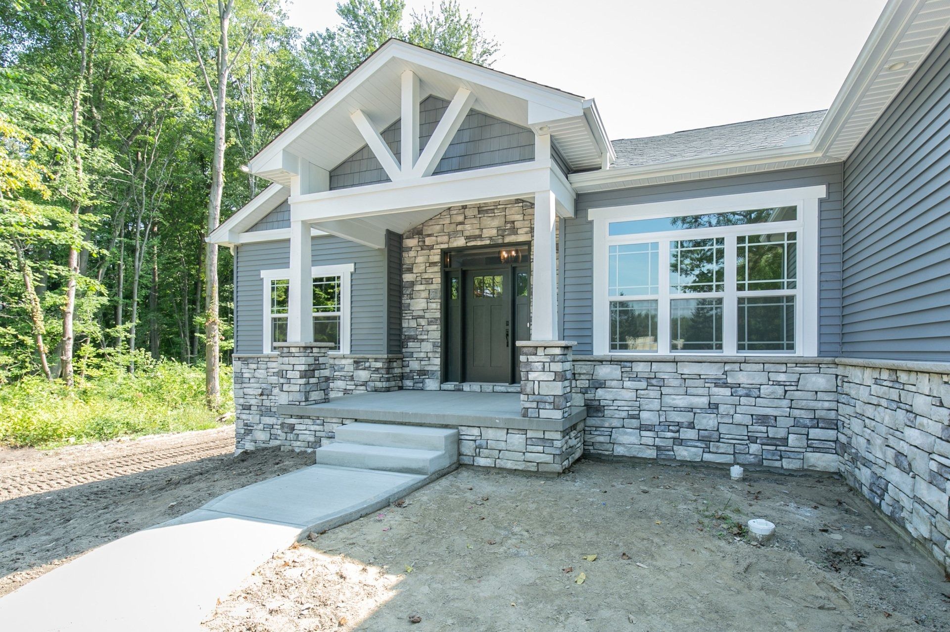 Gray house with stone accents, a concrete path, and a porch under a gable.