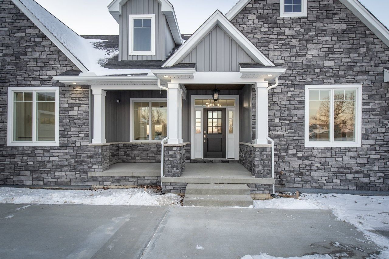 Gray stone house with white trim, snow, and a concrete pathway.