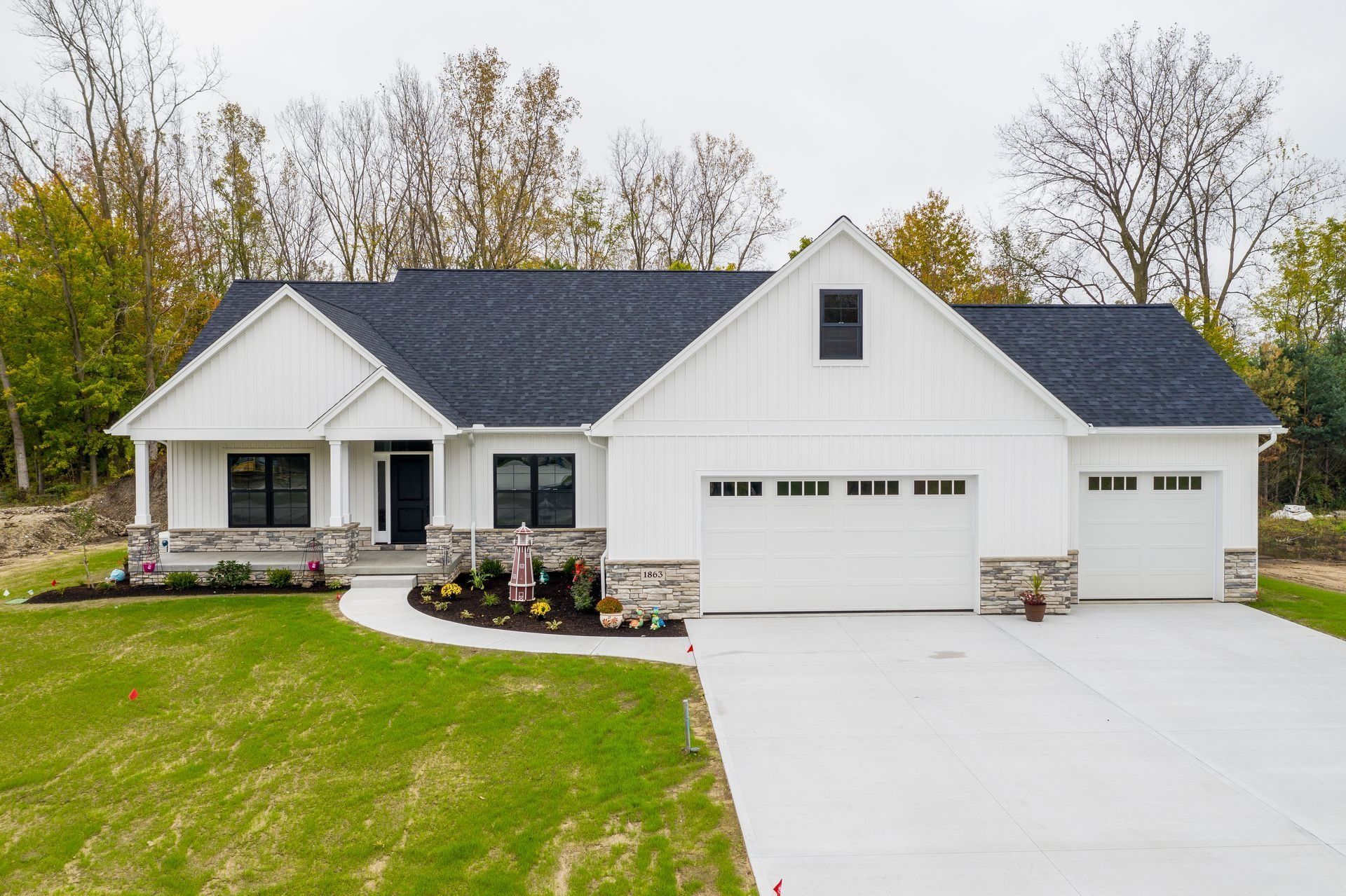 White modern farmhouse with black roof, gray stone accents, and two-car garage.