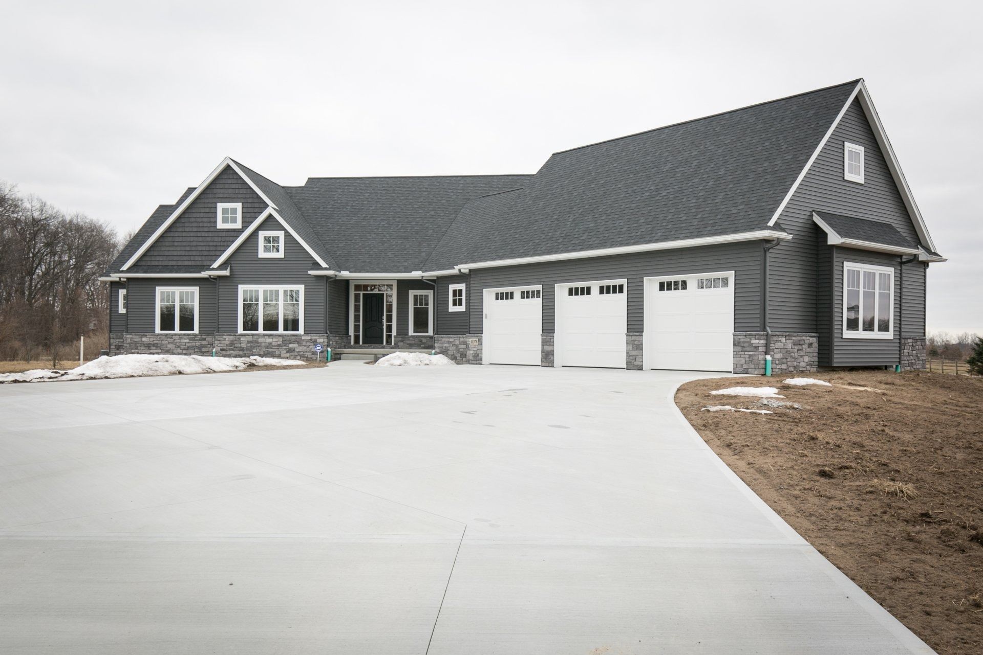 Gray house with a three-car garage and concrete driveway under a cloudy sky.