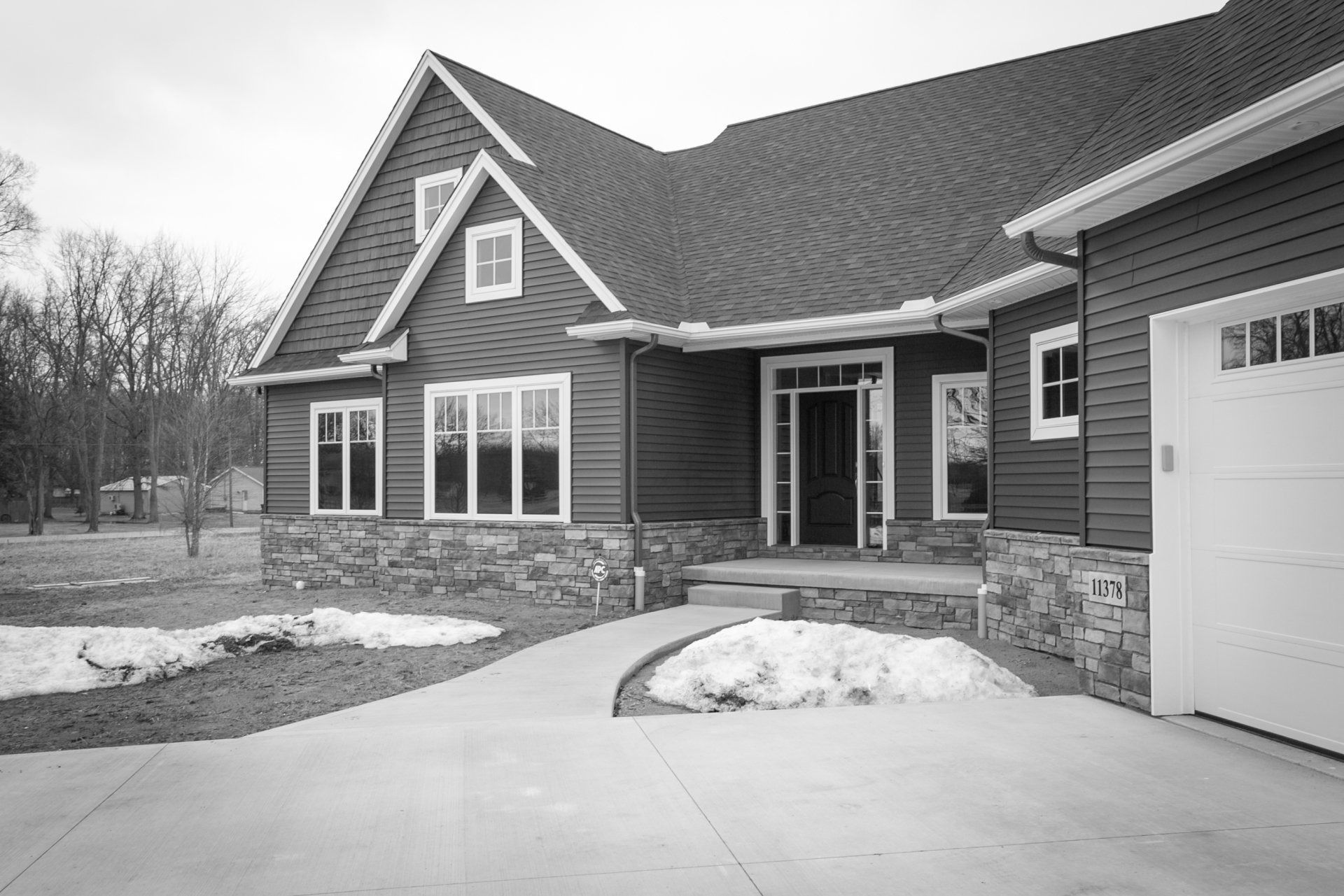 Exterior of a brown house with stone accents, a porch, a curved driveway, and a garage door.