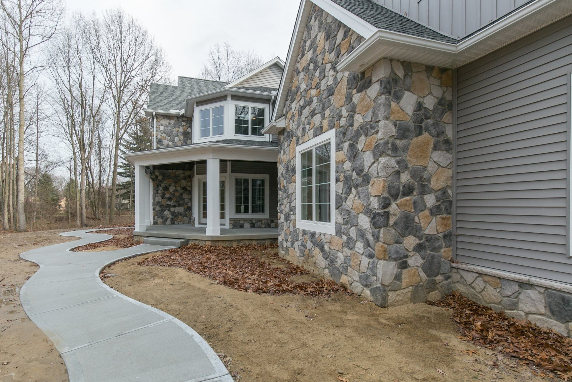 House with stone facade and gray siding, concrete walkway in front.