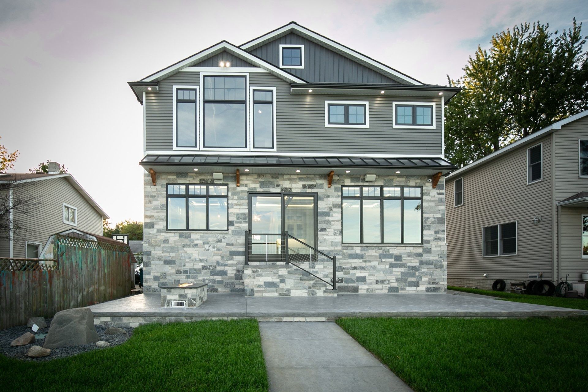 Two-story house with gray stone and siding facade, large windows, and a green lawn.