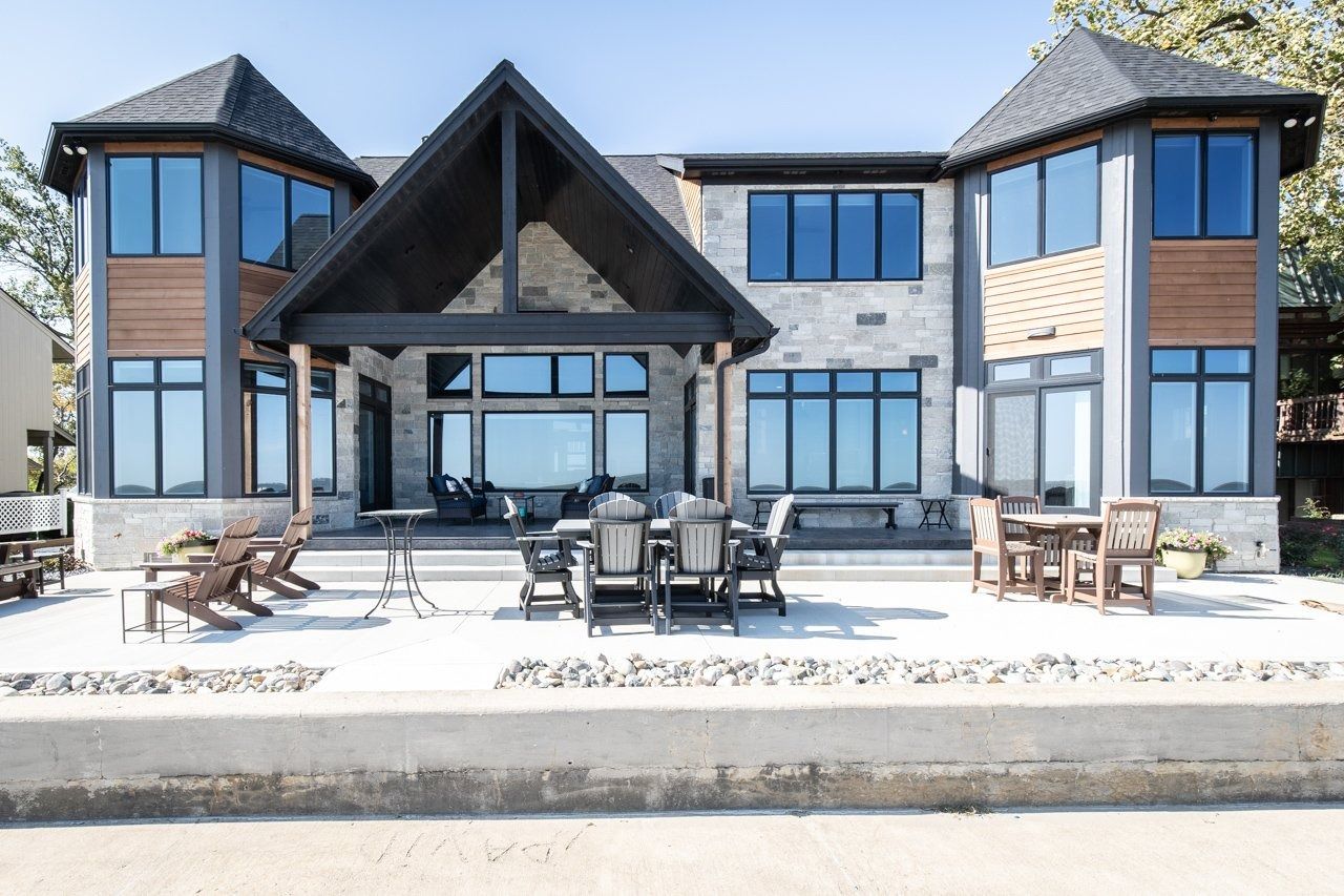 Waterfront home with stone and wood exterior, large windows, and patio furniture.