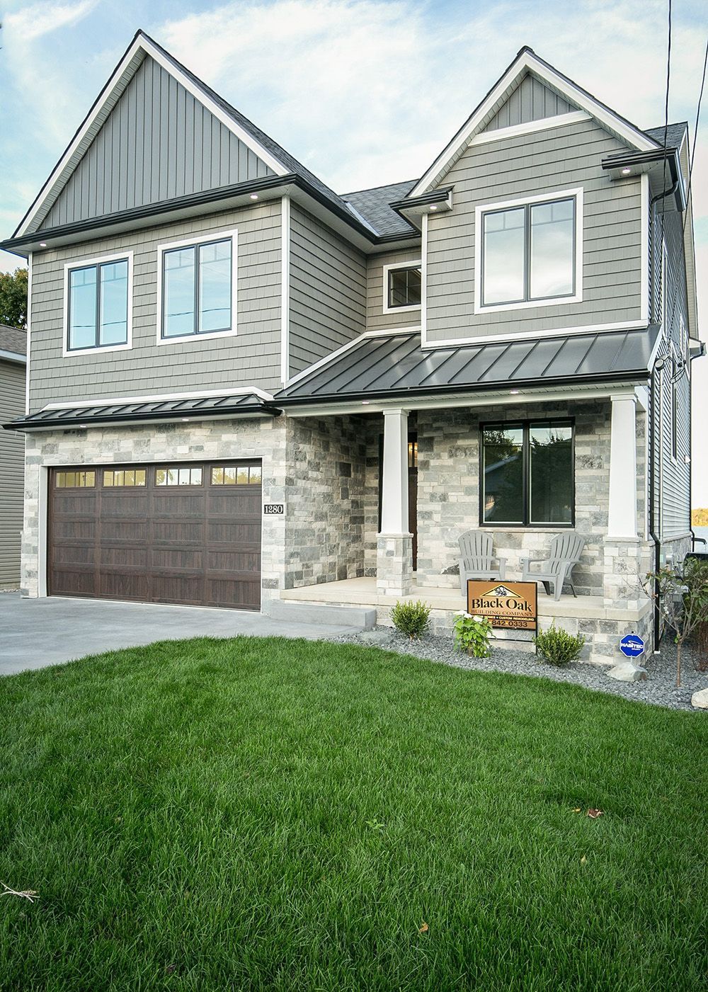 Two-story house with gray siding, stone facade, brown garage door, and lush green lawn.