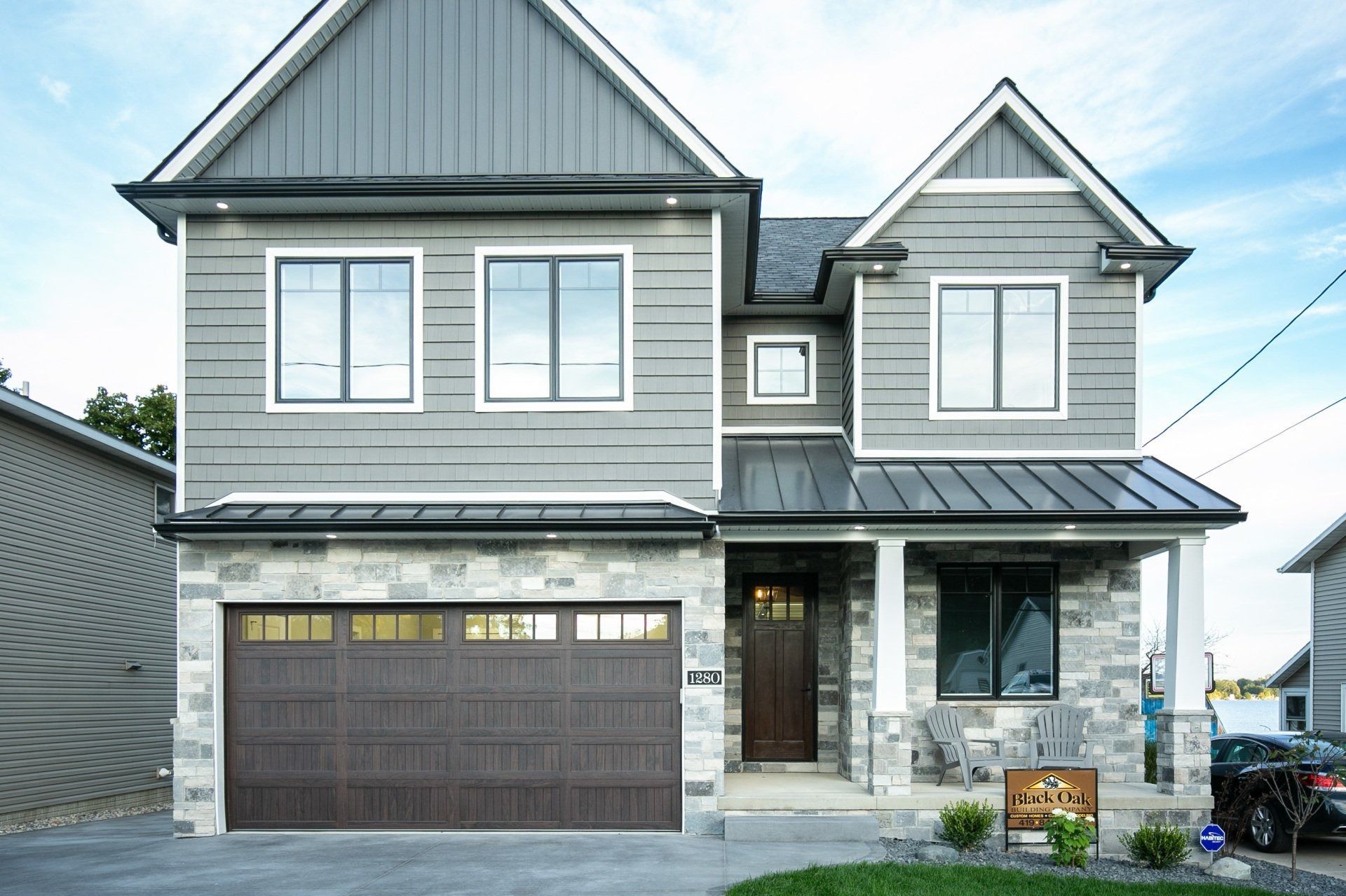 Gray two-story house with stone facade, brown garage door, and a small front yard.