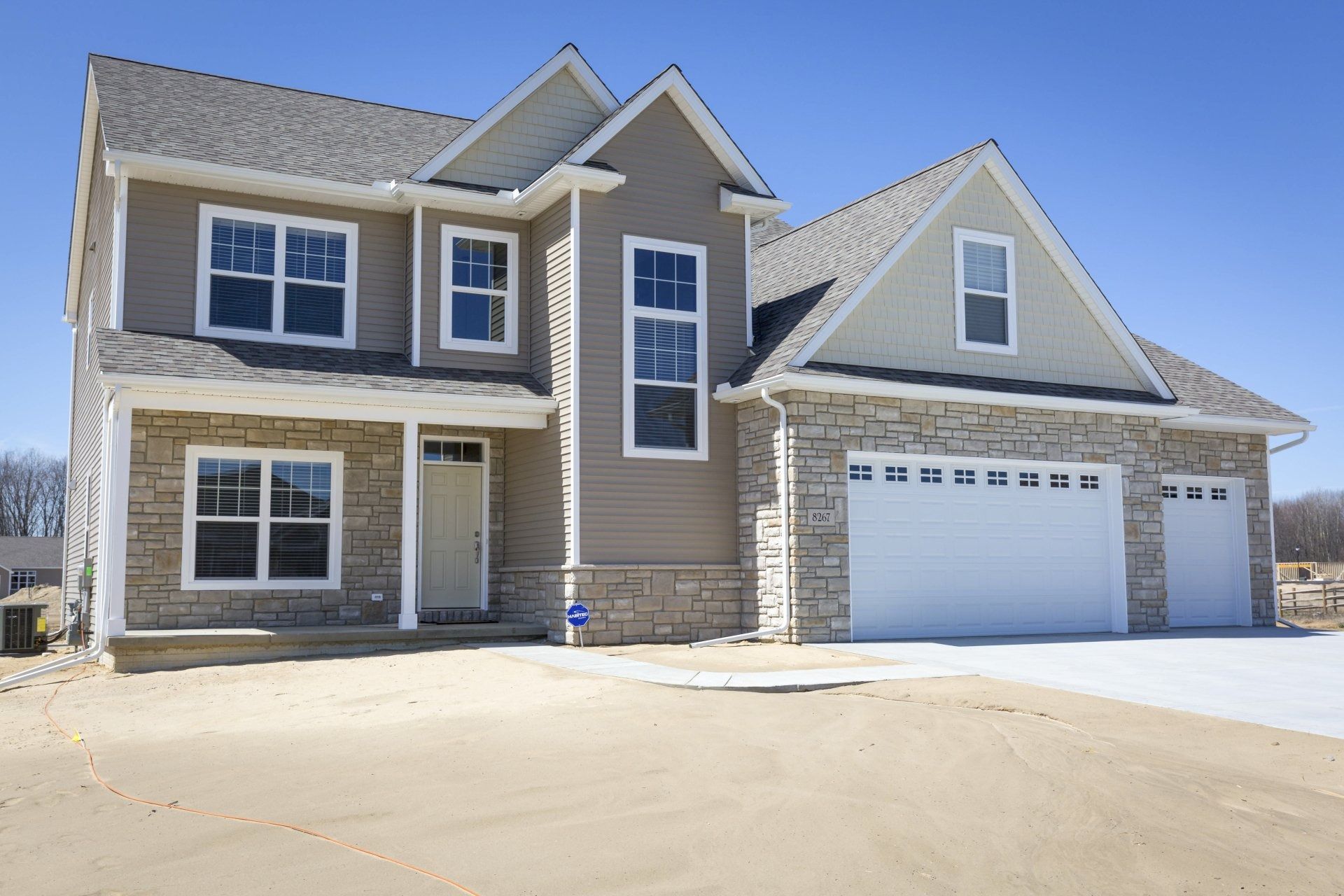Two-story house with stone and beige siding, gray roof, and three-car garage on a sunny day.