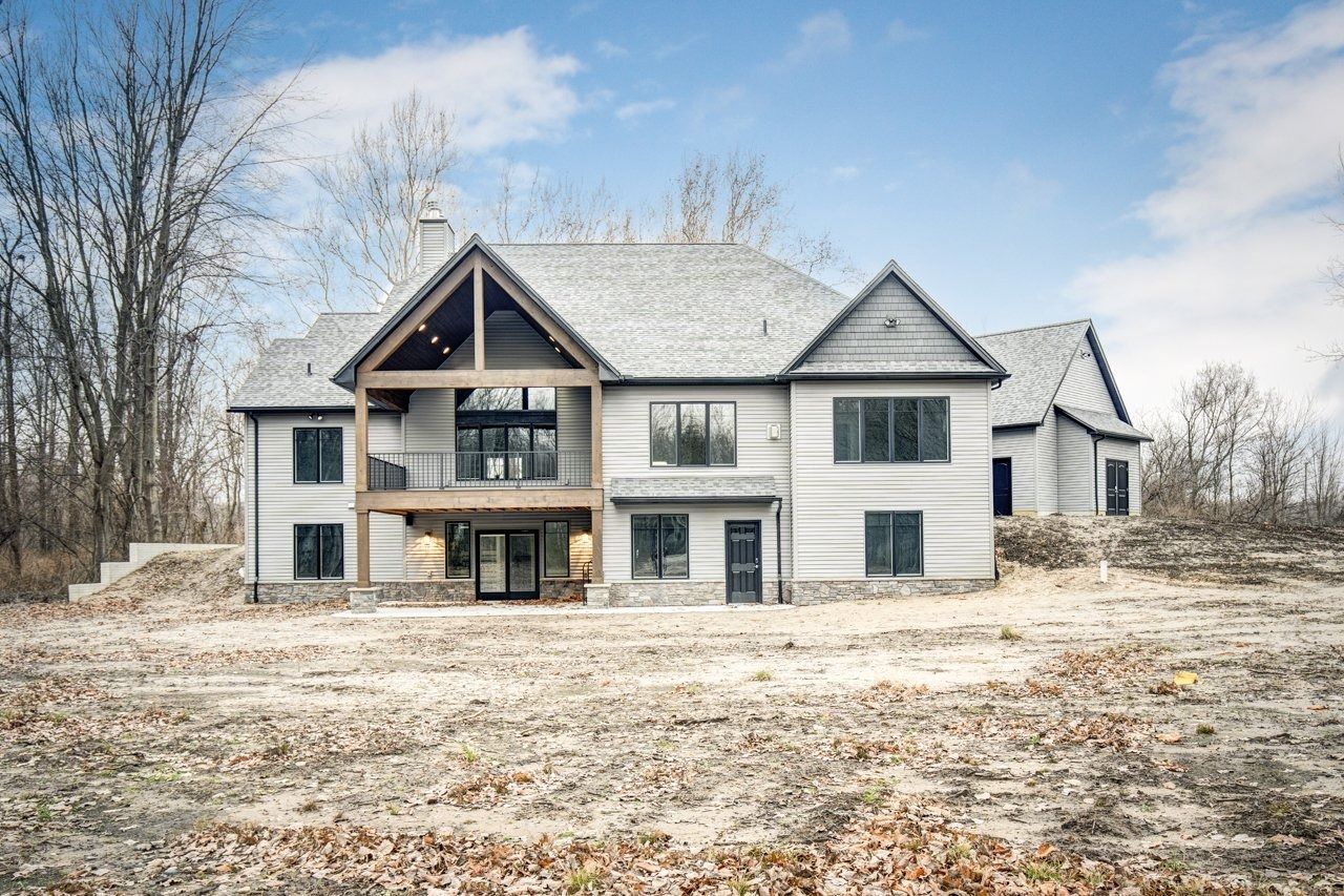 Gray modern house with an open balcony on a hillside under a blue sky.
