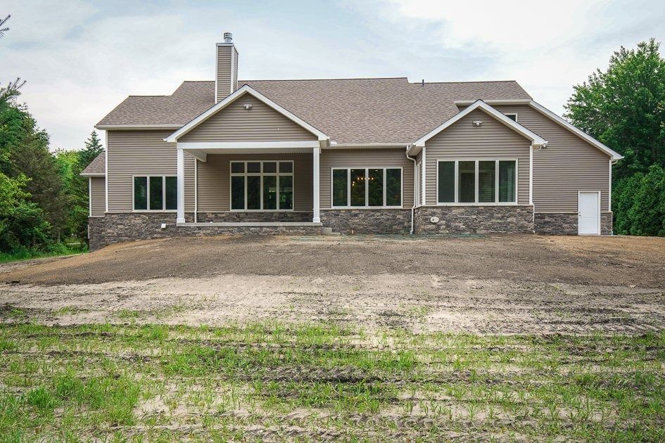Tan and stone house with windows and a covered porch, set on a graded lot with emerging grass.