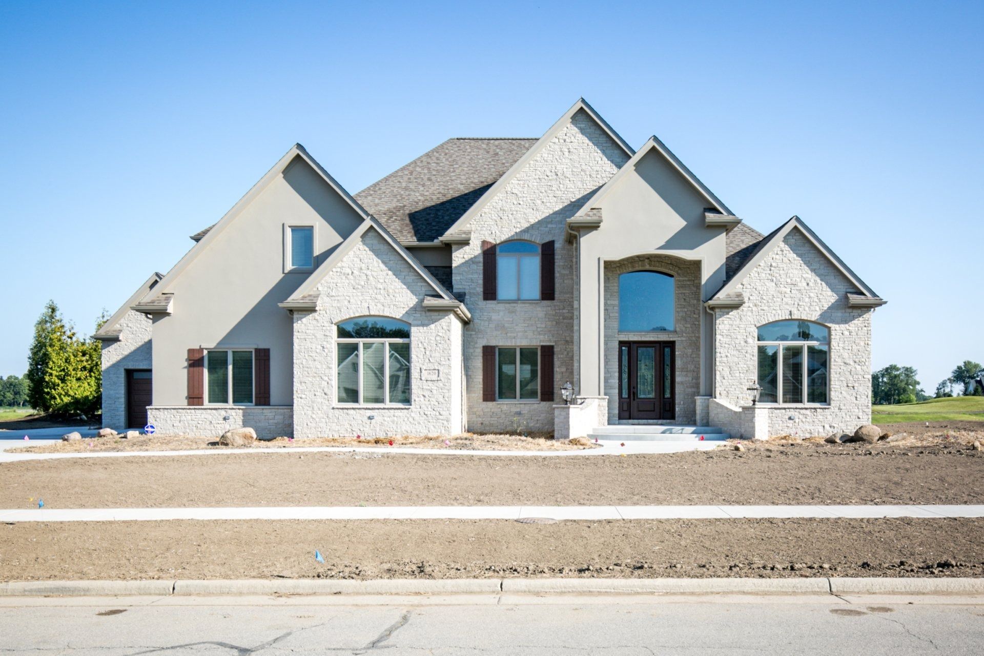 Large, two-story house with gray stone and light stucco exterior on a sunny day. Brown shutters and front door.