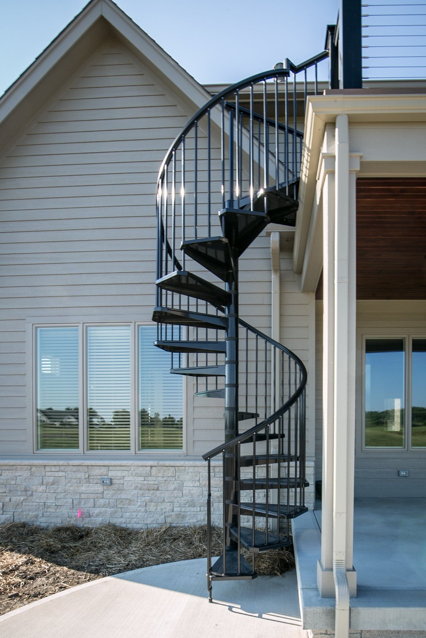Black spiral staircase outside a light-colored building with large windows and a porch.