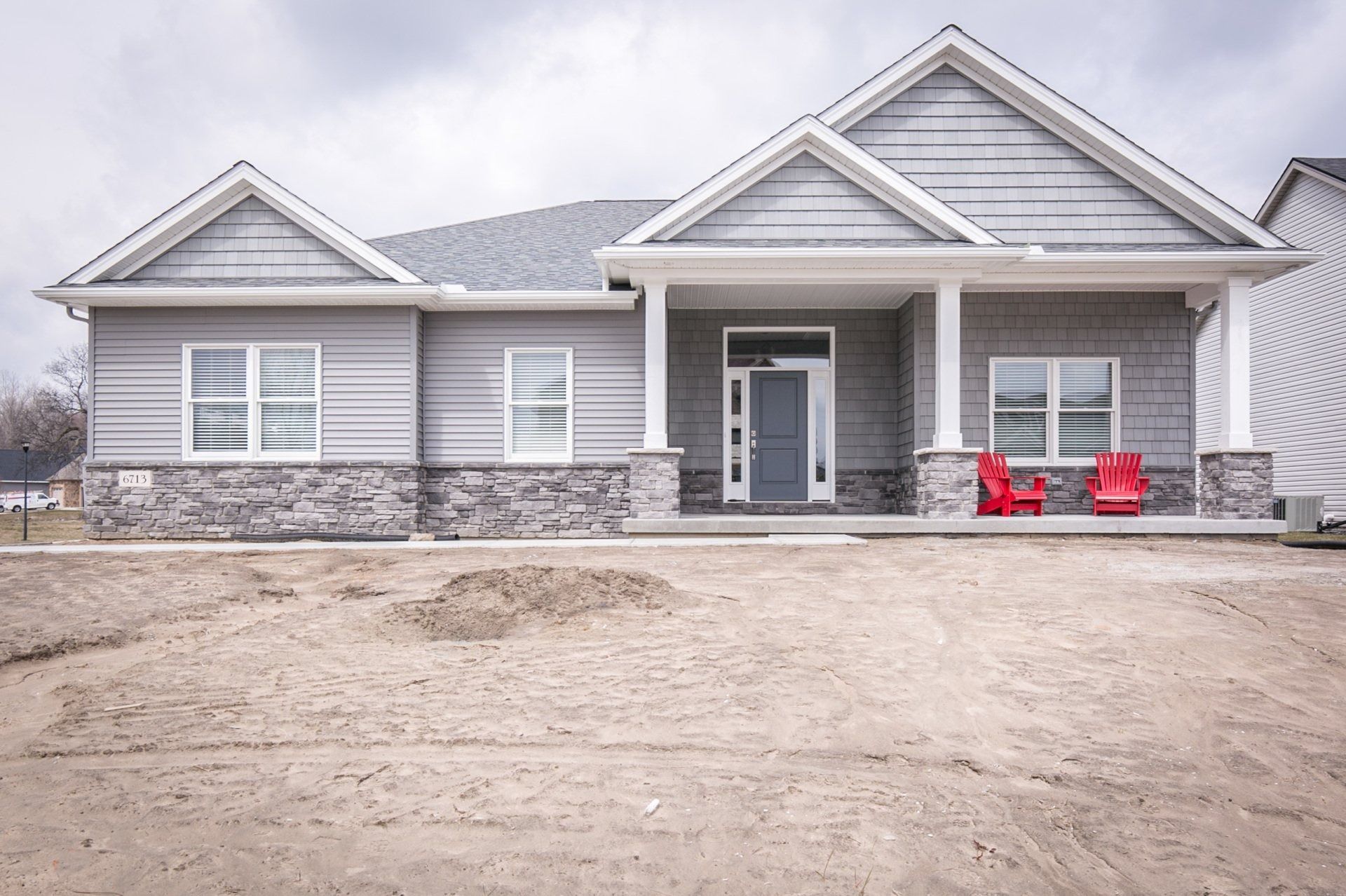 Gray house with stone accents, a covered porch, and two red chairs on the porch.