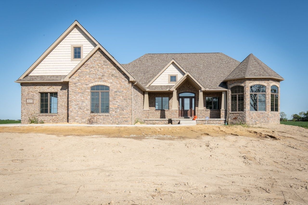 Brick house with brown roof, blue sky background, and bare dirt in front.