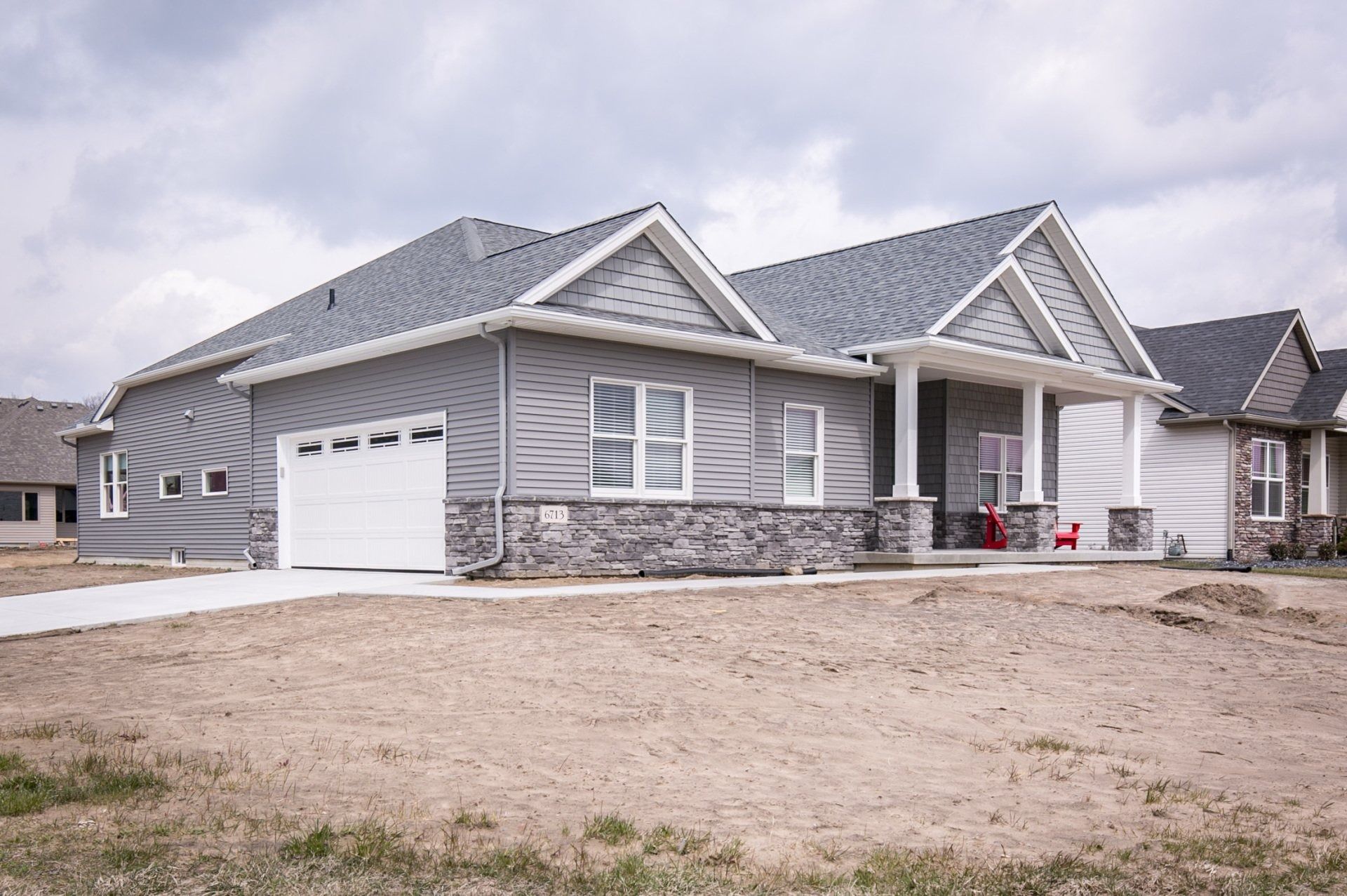 Gray house with a garage and porch, surrounded by dry land under a cloudy sky.
