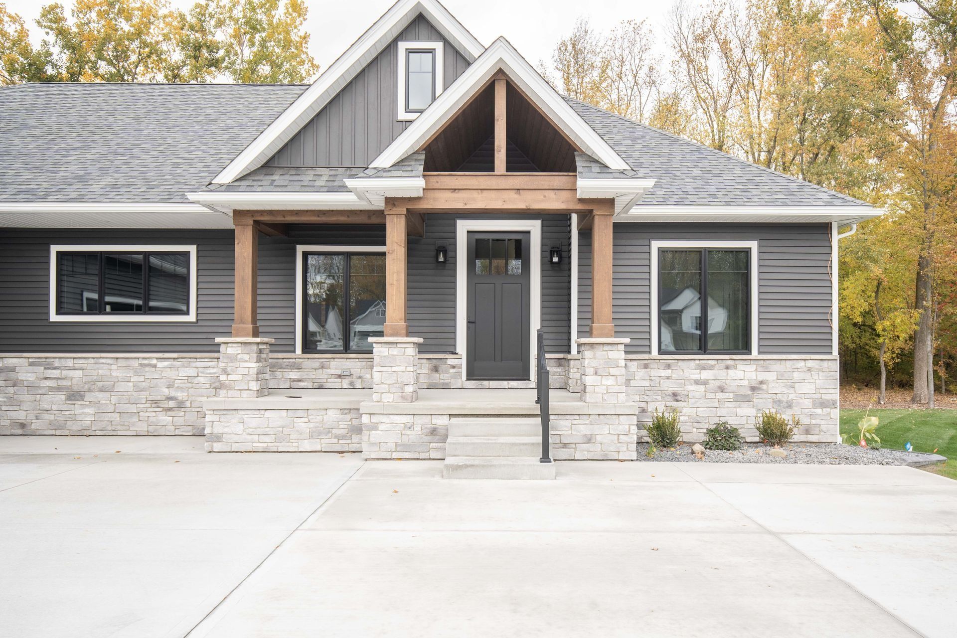 Modern gray house with stone facade, wooden porch, and dark front door.