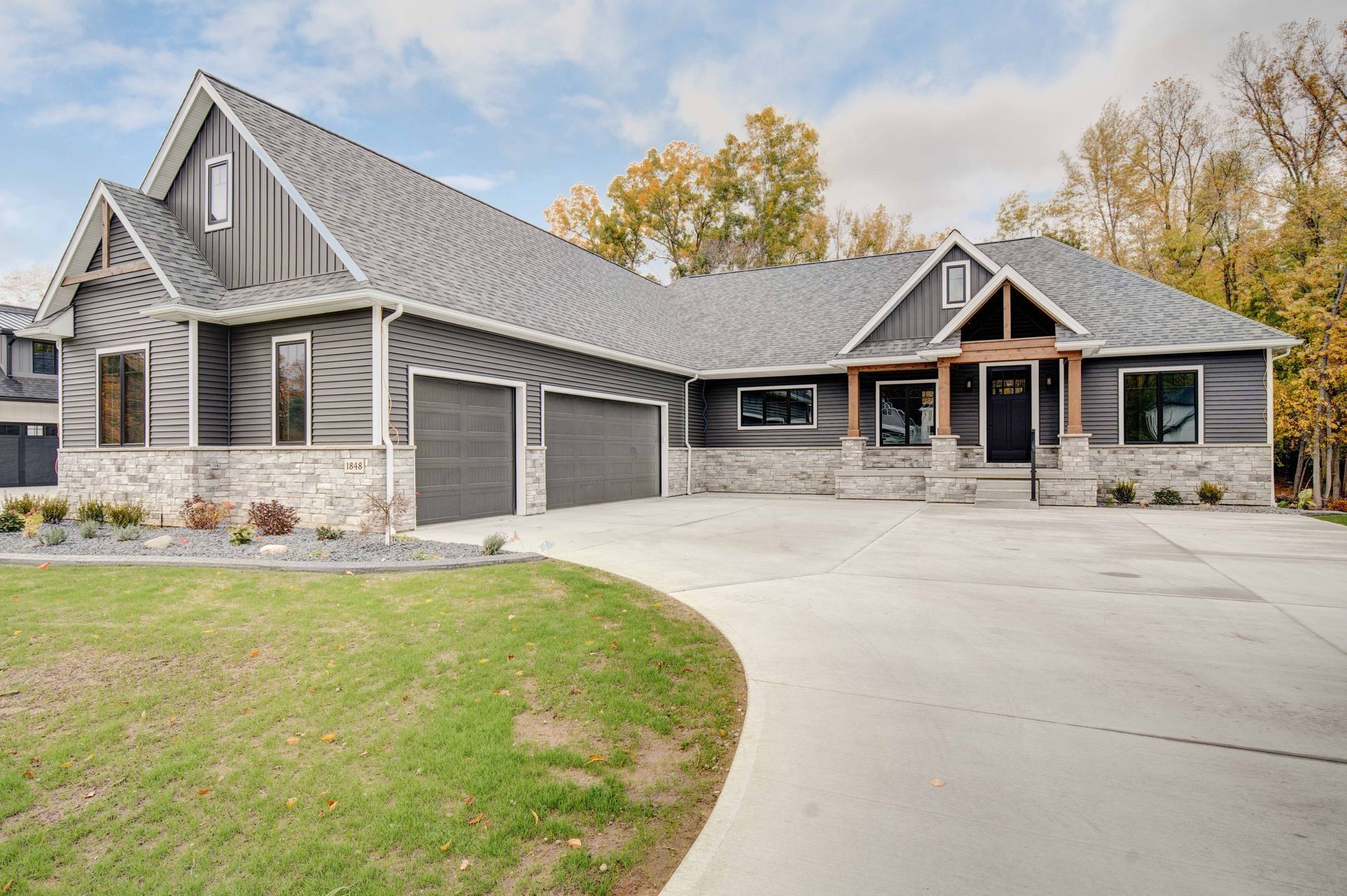 Modern gray home with stone accents, two-car garage, and curved driveway on a cloudy day.