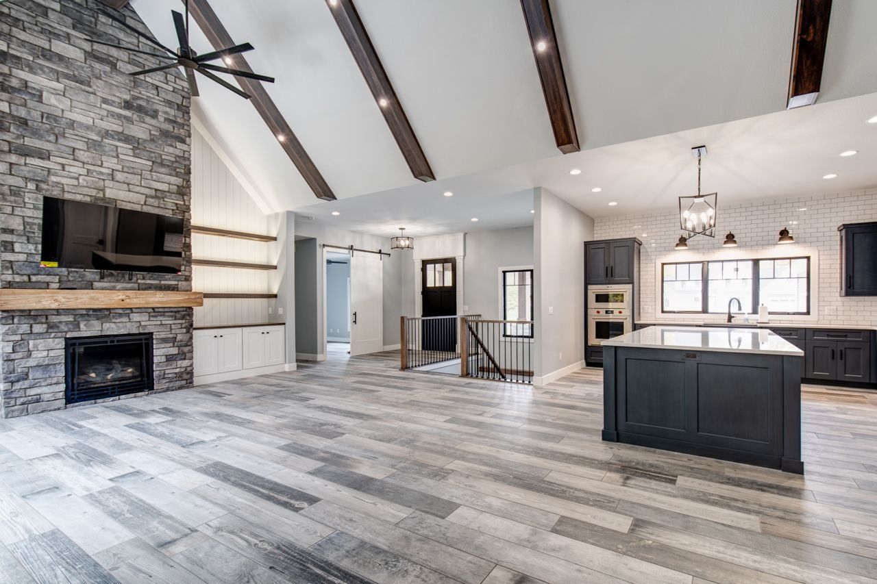 Spacious modern living room with fireplace and kitchen, grey floors and dark cabinetry.