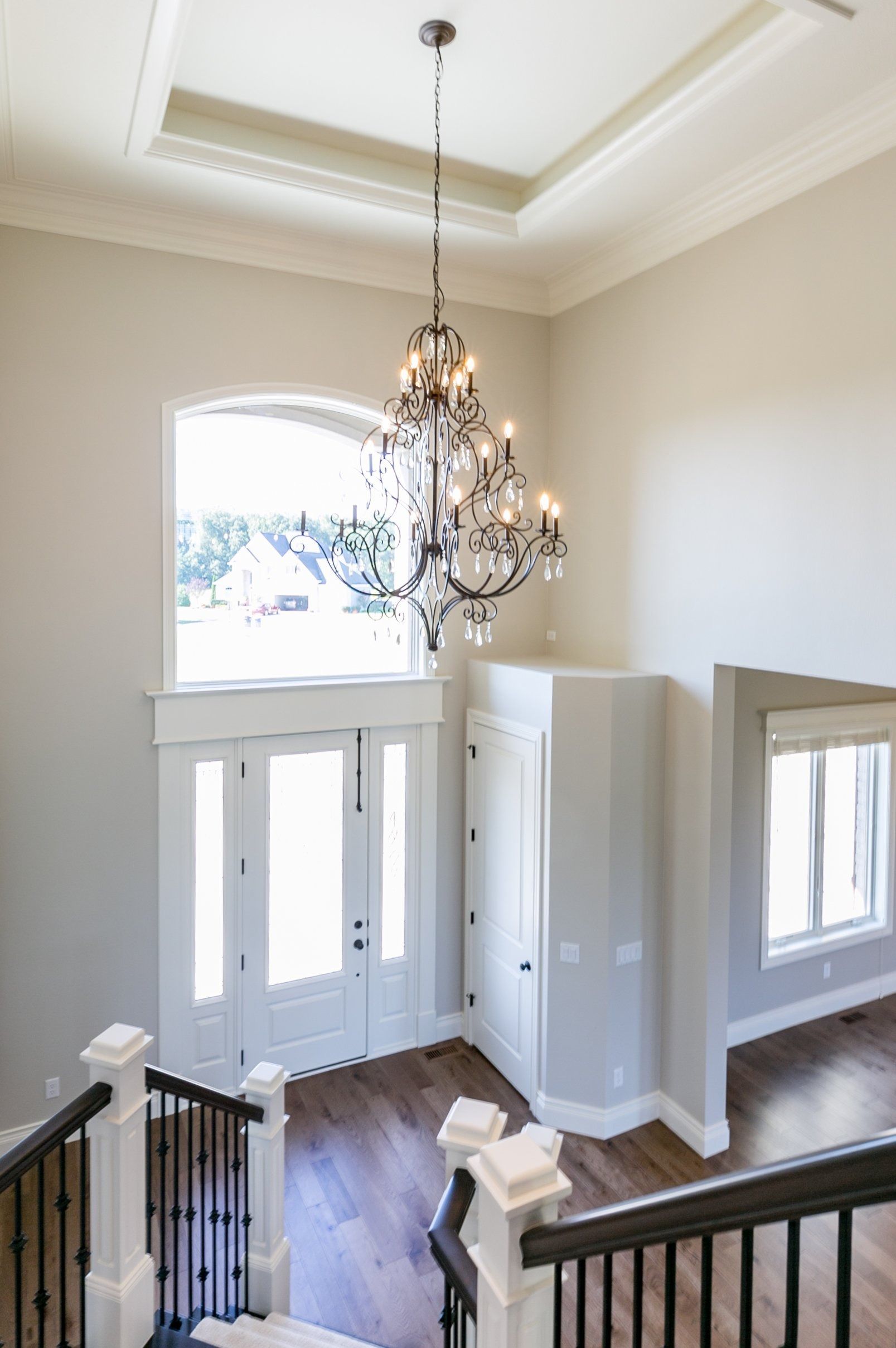 Entryway with chandelier, staircase, front door, and windows; neutral colors, wood flooring.