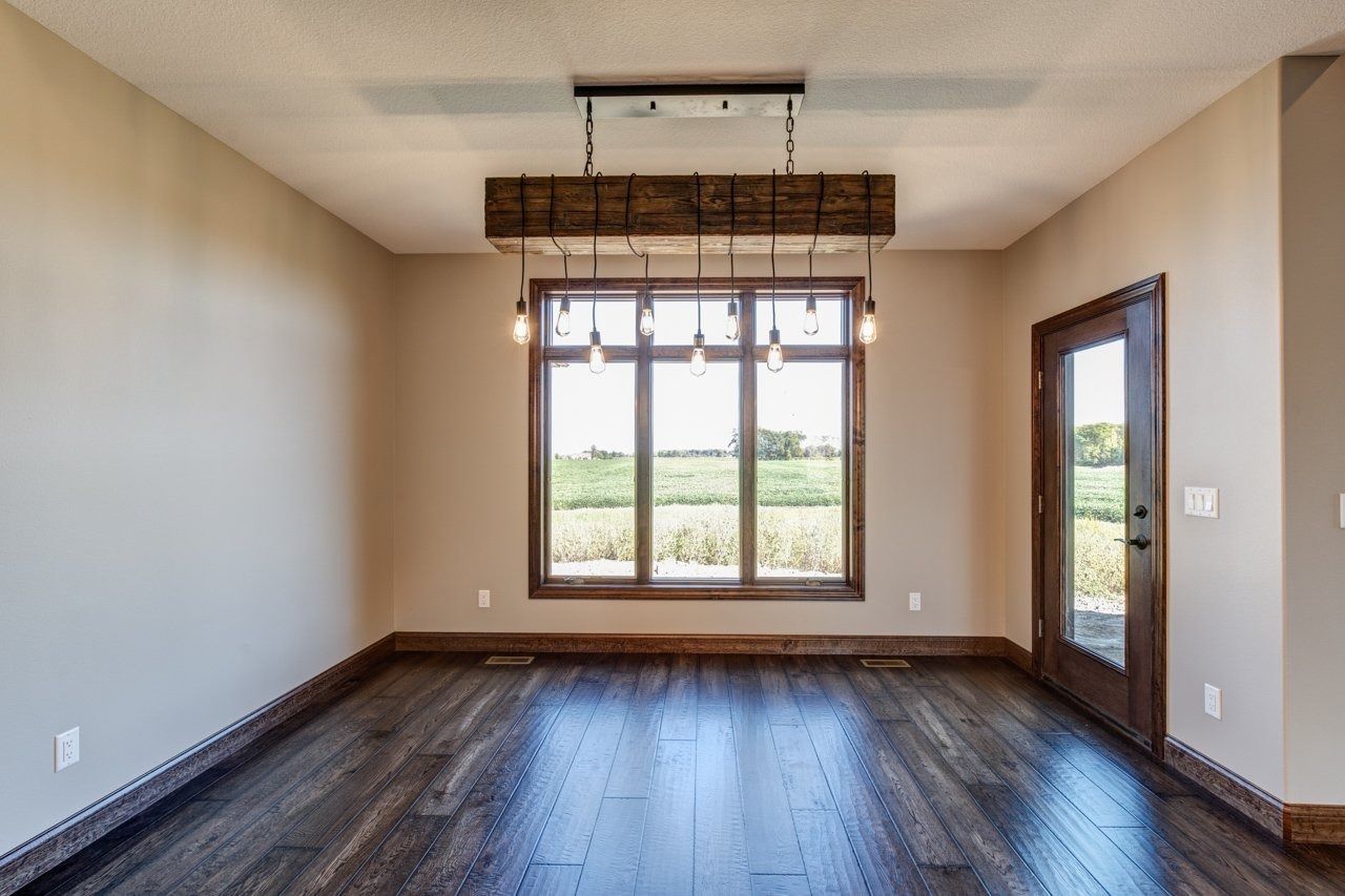 Empty dining room with dark wood floors, large window, and wooden light fixture.