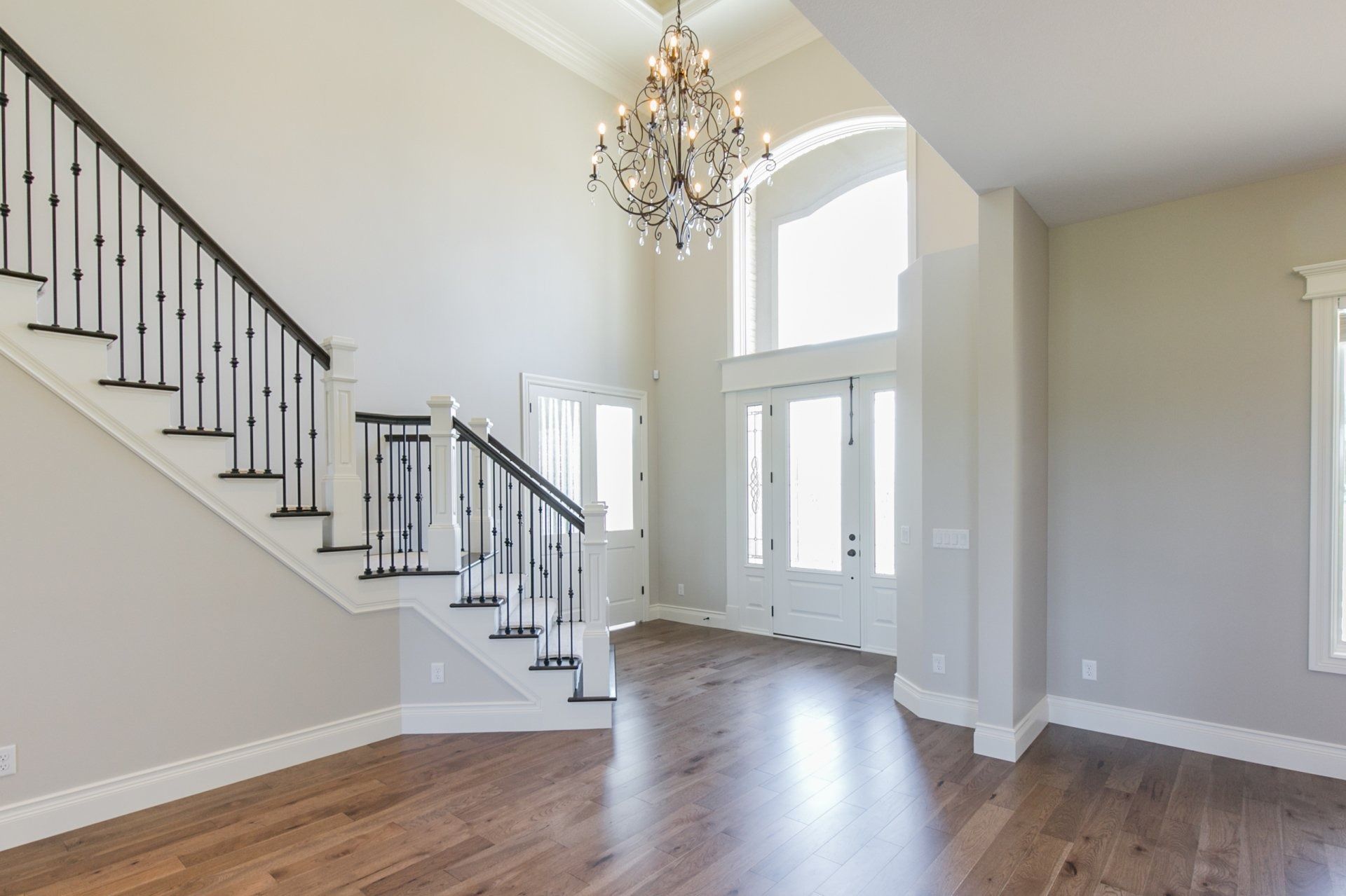 Bright entryway with staircase, chandelier, and double doors; hardwood floors and white walls.