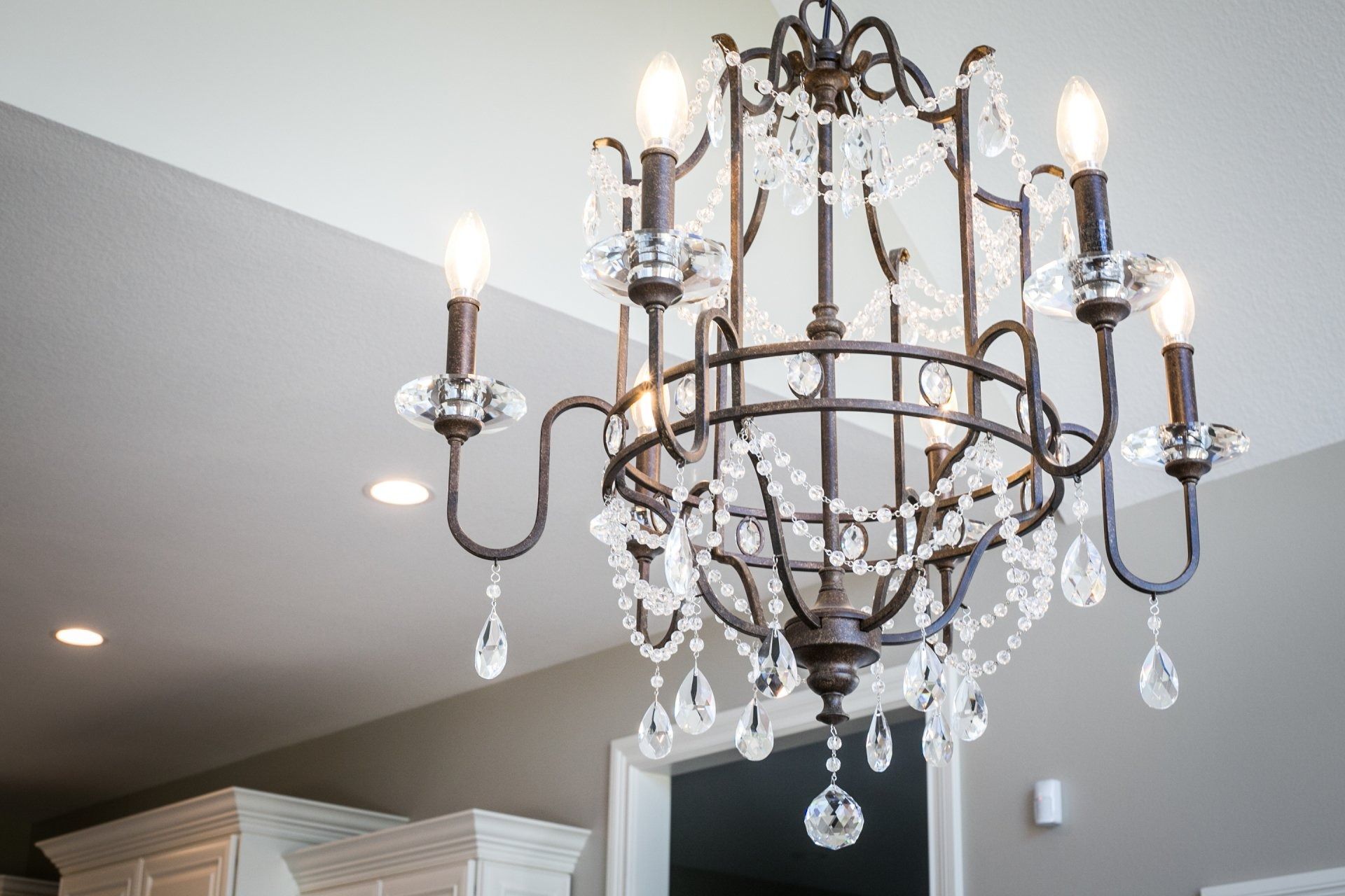 Ornate chandelier with crystals hanging from a white ceiling, above a kitchen counter.