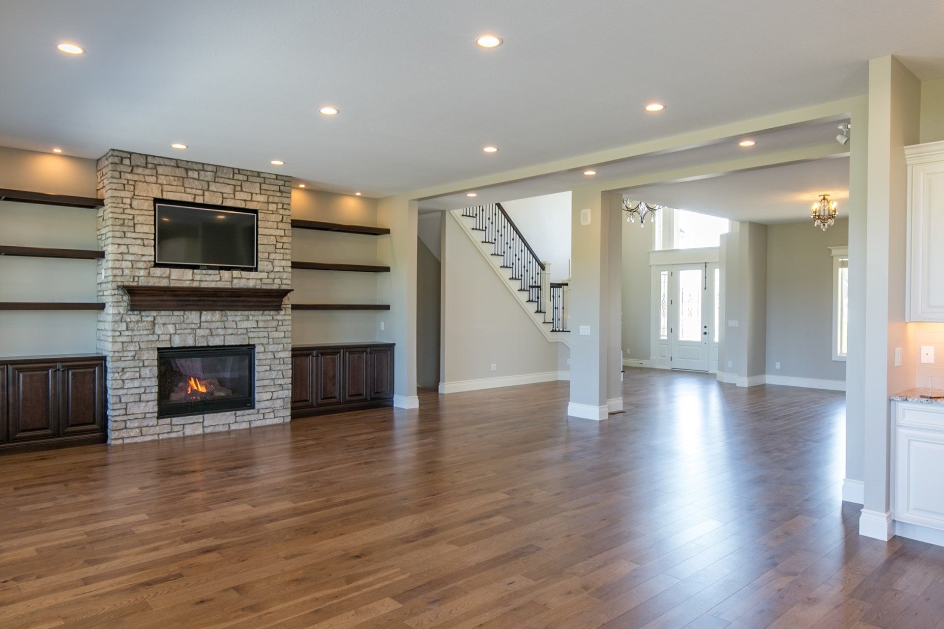 Spacious living room with stone fireplace, built-in shelves, hardwood floors, and staircase.