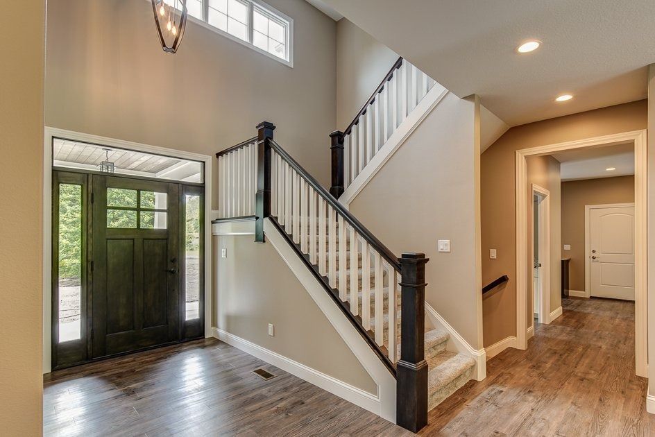 Entryway with dark wood door, staircase with white railing, and wood flooring.