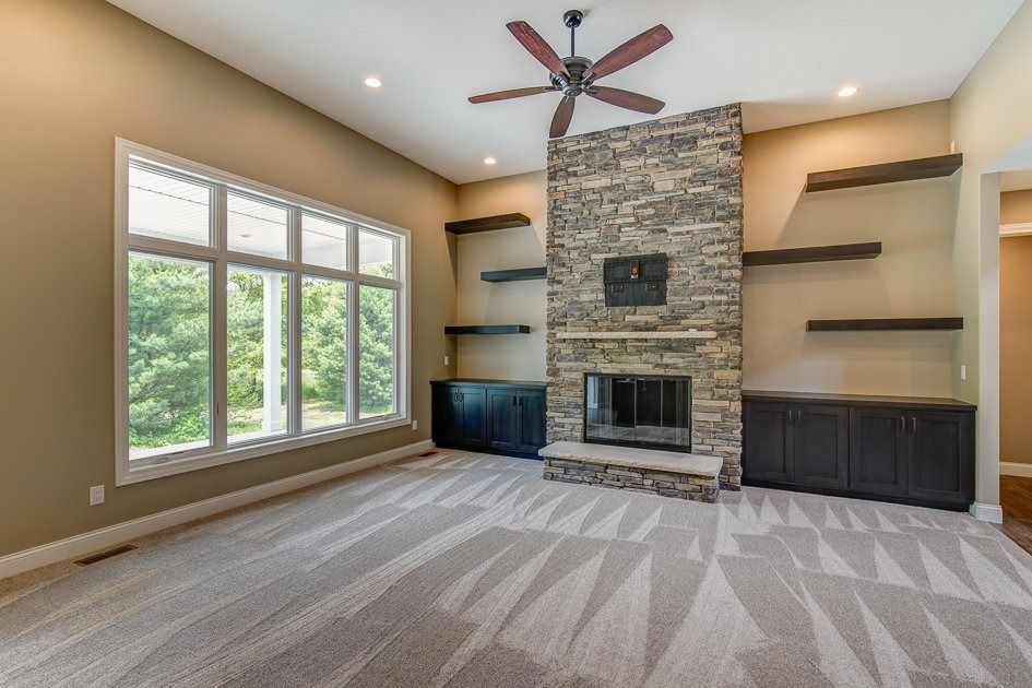 Living room with stone fireplace, built-in shelves, large window, and patterned carpet.