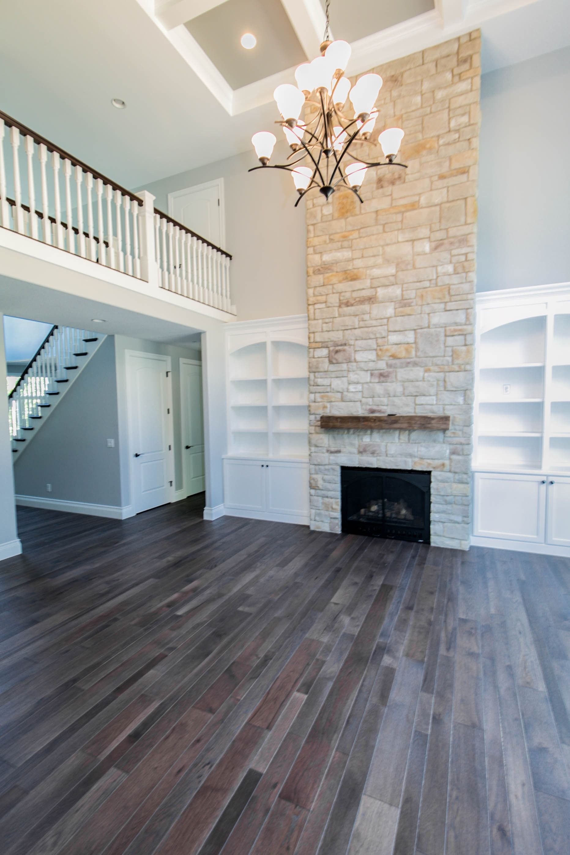 Spacious living room with stone fireplace, built-in bookshelves, dark wood floors, and a balcony.