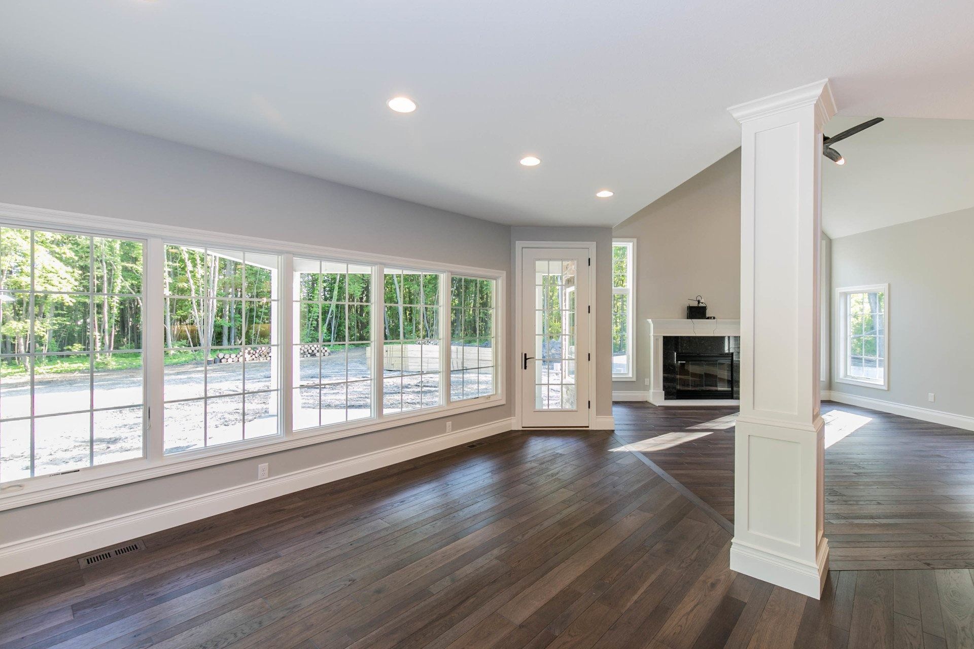 Spacious room with large windows, dark wood floor, fireplace, and a white pillar.