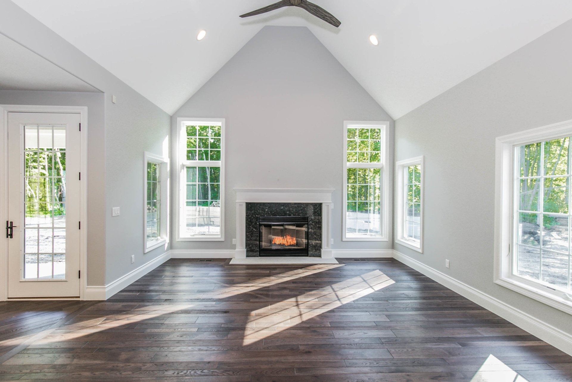 Empty living room with fireplace, vaulted ceiling, windows, and dark wood floors.