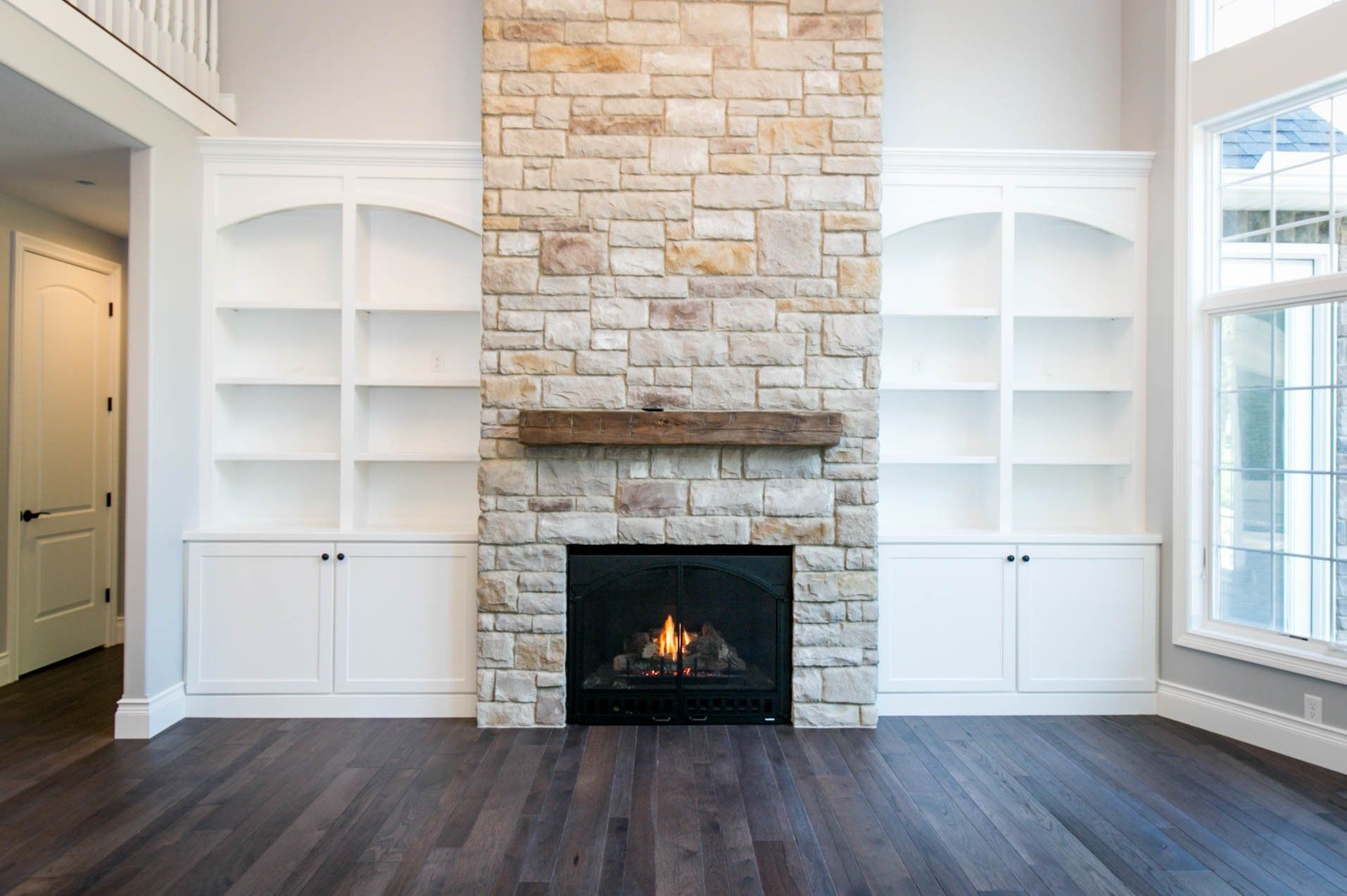 Fireplace with stone surround, flanked by white bookshelves, in a room with hardwood floors.