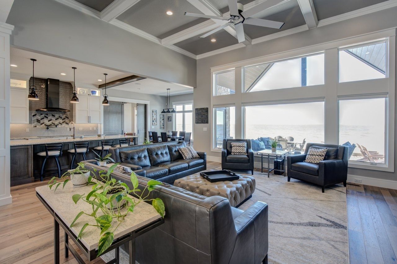 Open-concept living space with a kitchen, living room, and large windows; gray and white color scheme; leather furniture.