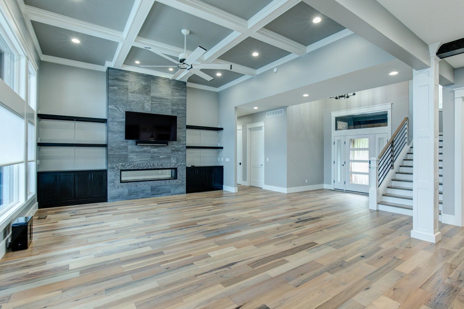 Spacious modern living room with fireplace, built-ins, and light wood floors. Gray walls and coffered ceiling.