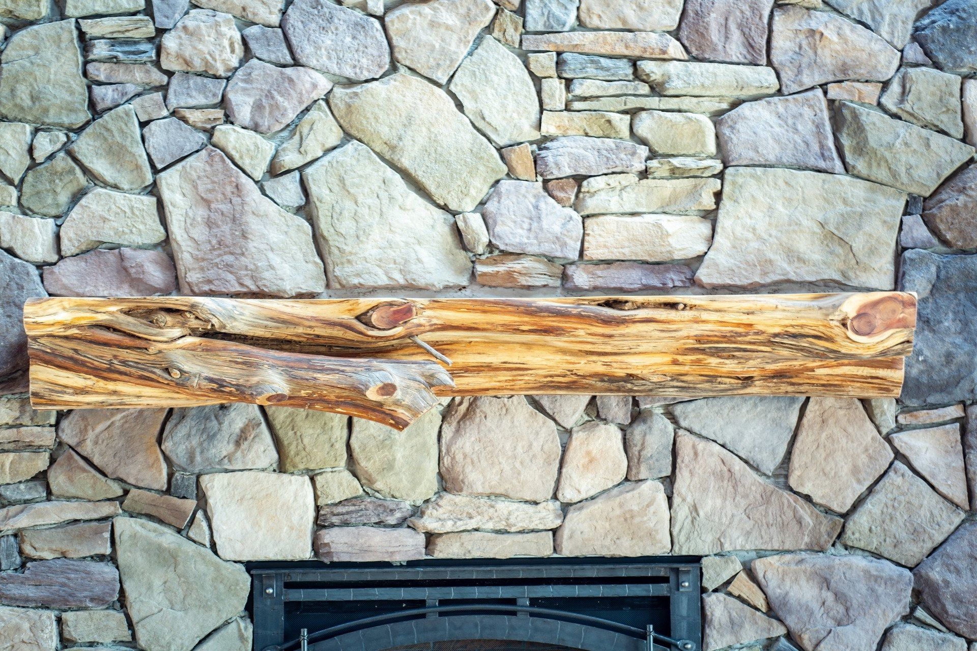 Wooden mantel on a stone fireplace above a black fireplace opening.