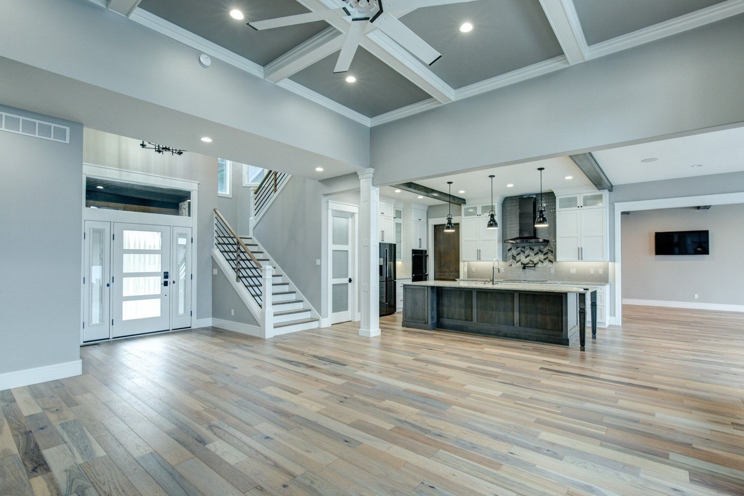 Spacious open-concept living area with light wood floors, a kitchen island, and a staircase.