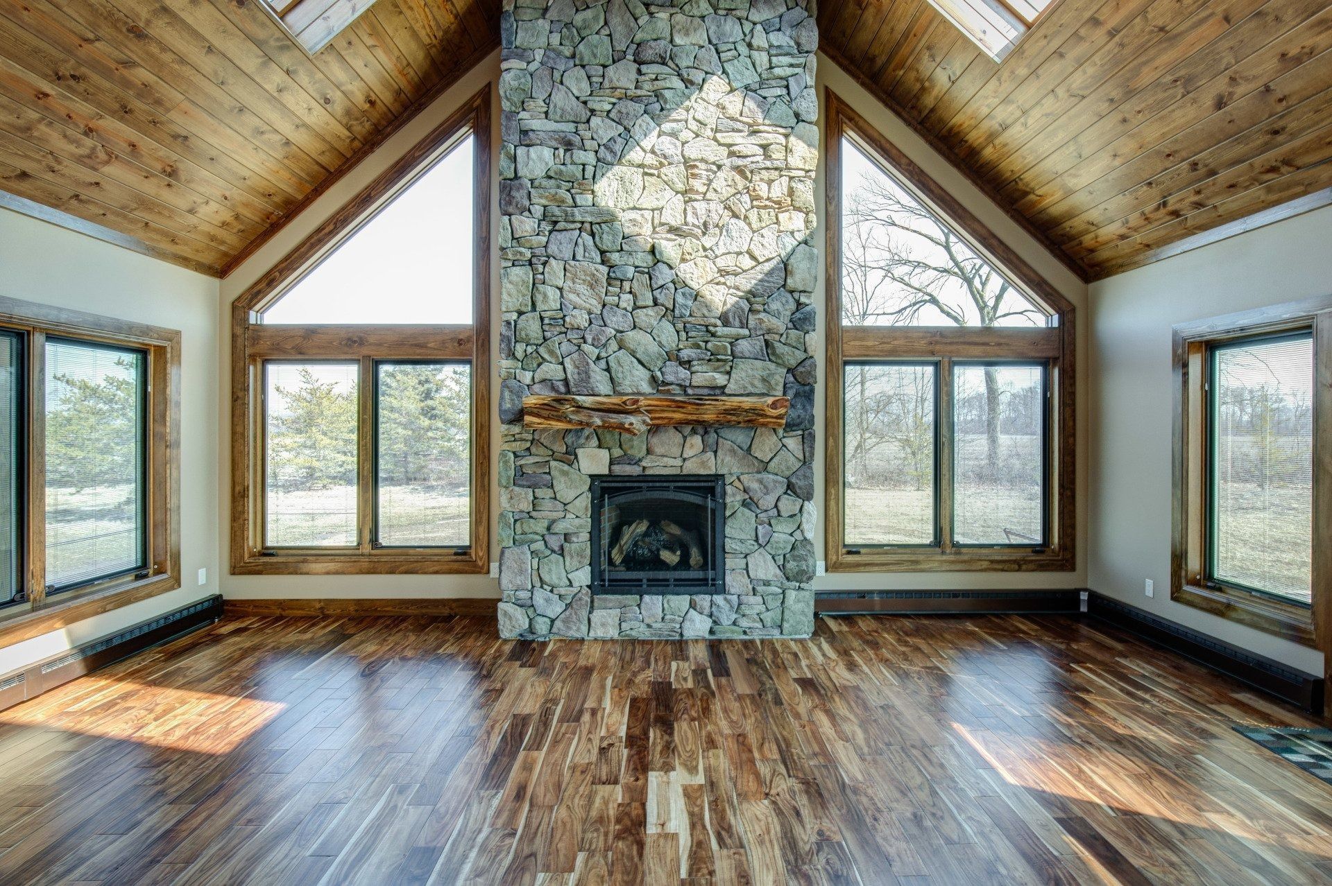 Spacious room with wood floor, stone fireplace, and large windows. Wooden ceiling.