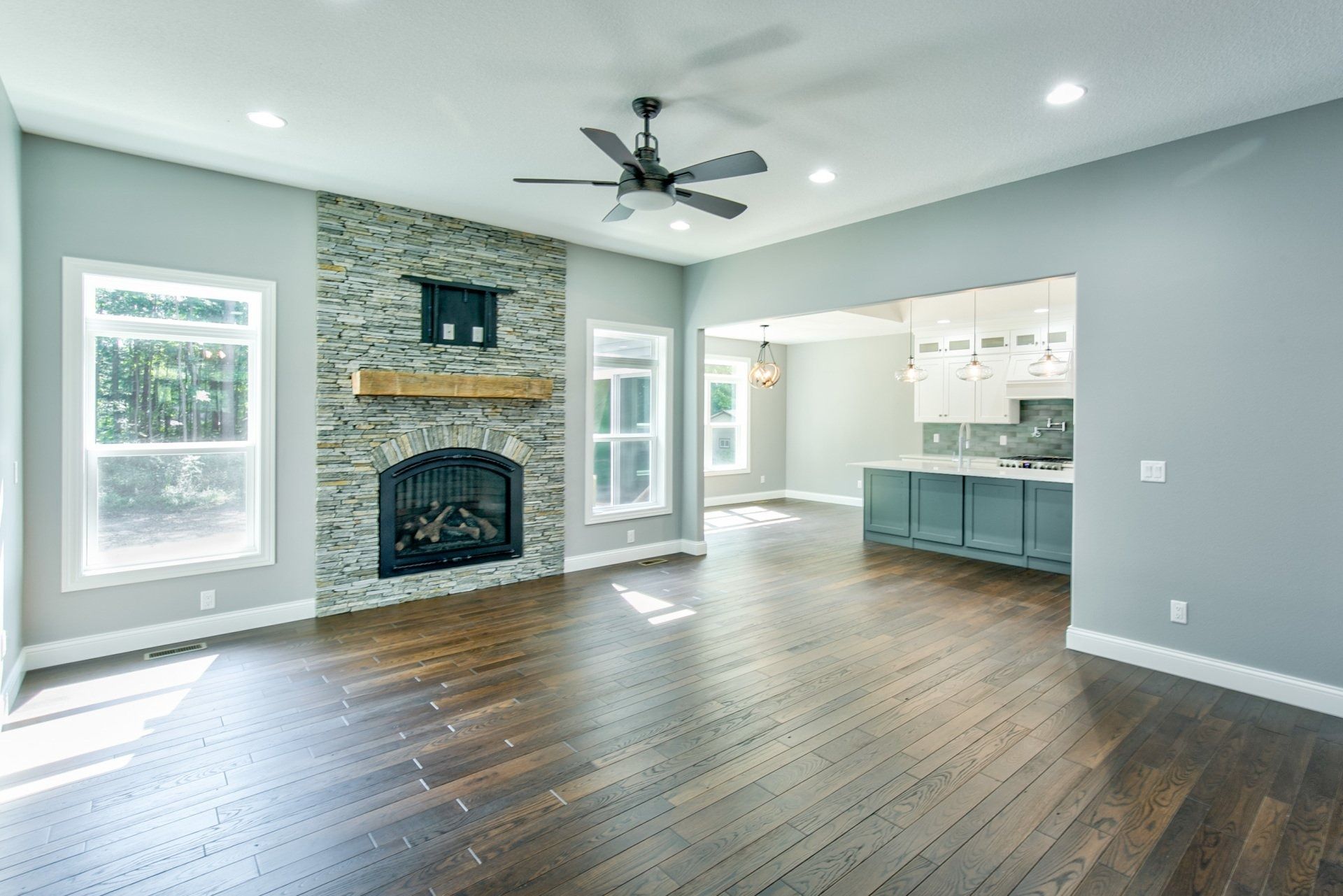 Spacious living room with stone fireplace, hardwood floors, and open concept to kitchen.