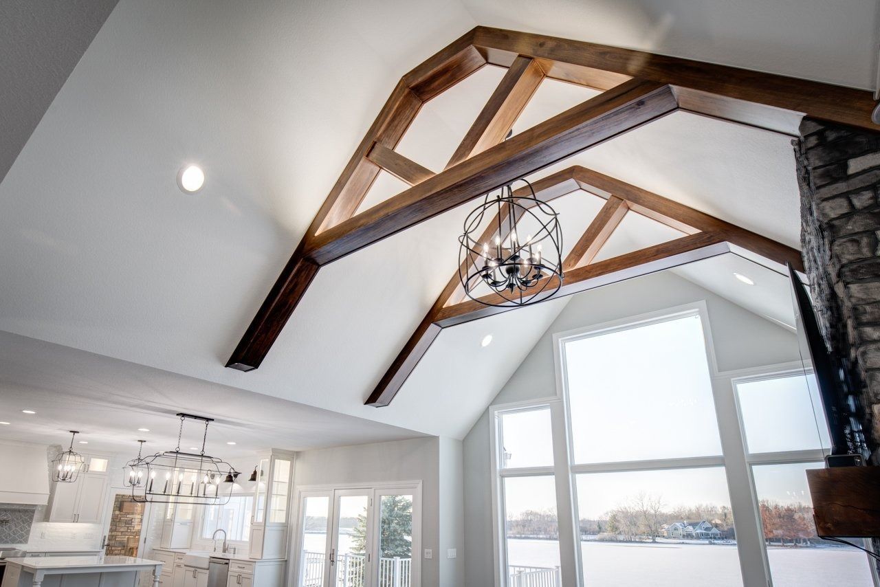 Vaulted ceiling with exposed wood beams, chandelier, and large windows overlooking a snowy landscape.
