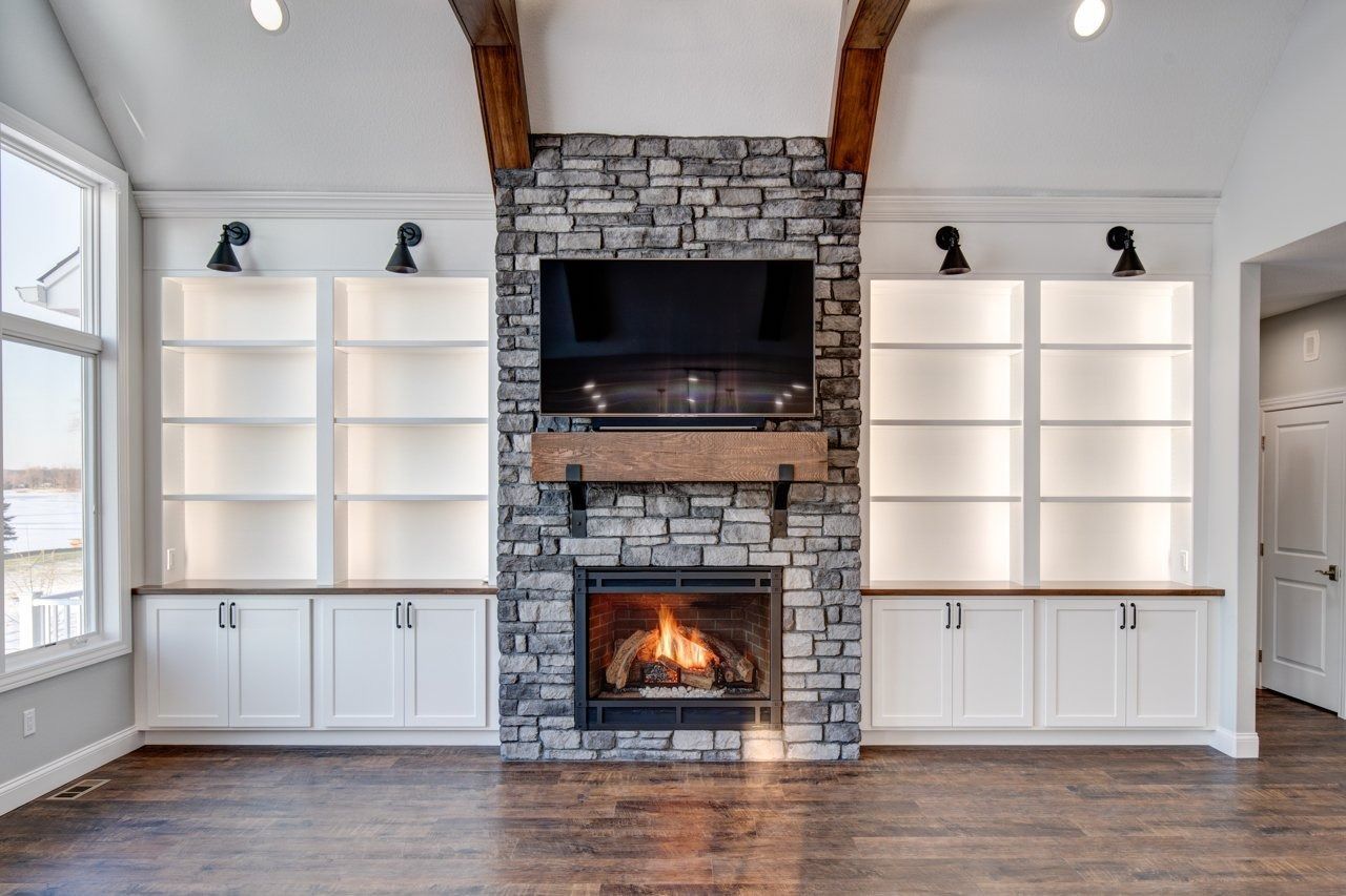 Living room with stone fireplace, TV, built-in white cabinets, and wooden beams.