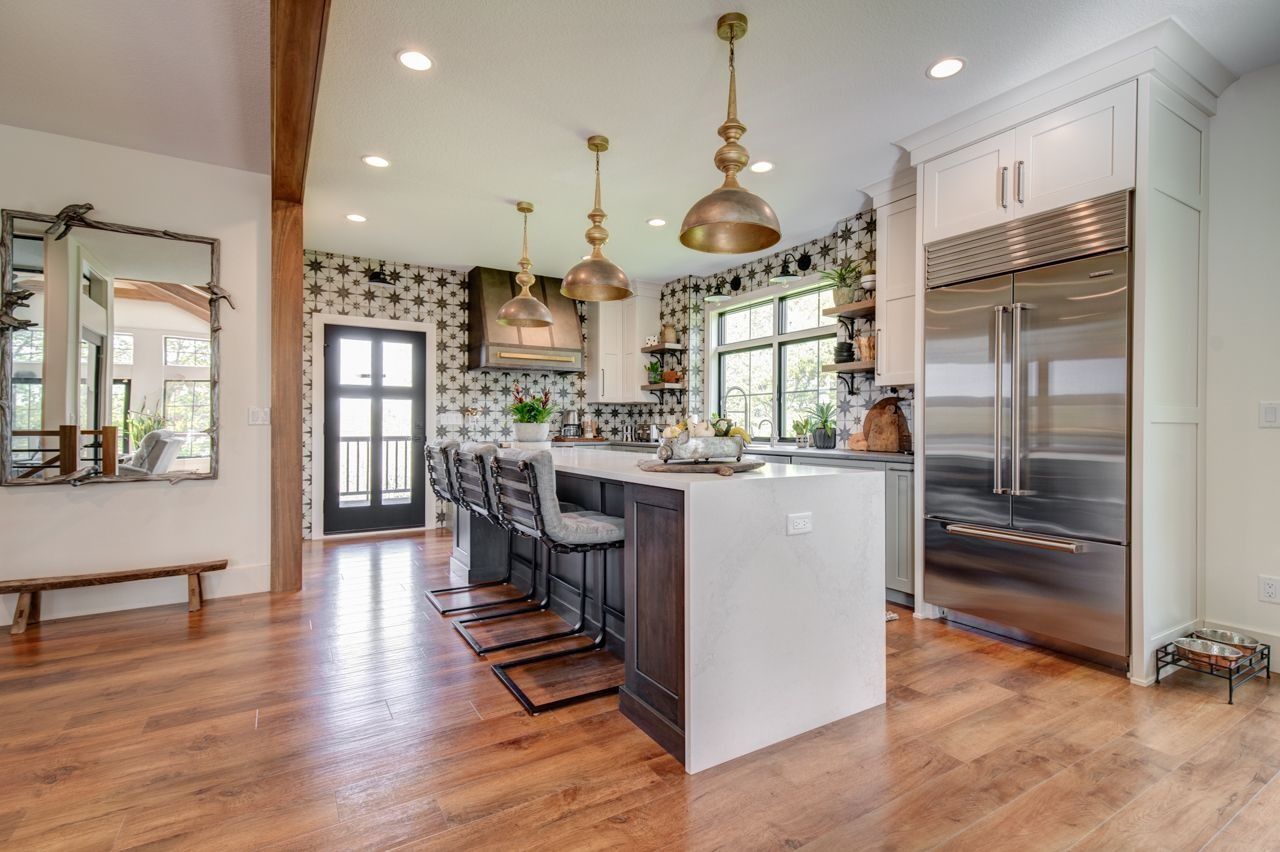 Modern kitchen with island, pendant lights, stainless steel refrigerator, and patterned wallpaper.