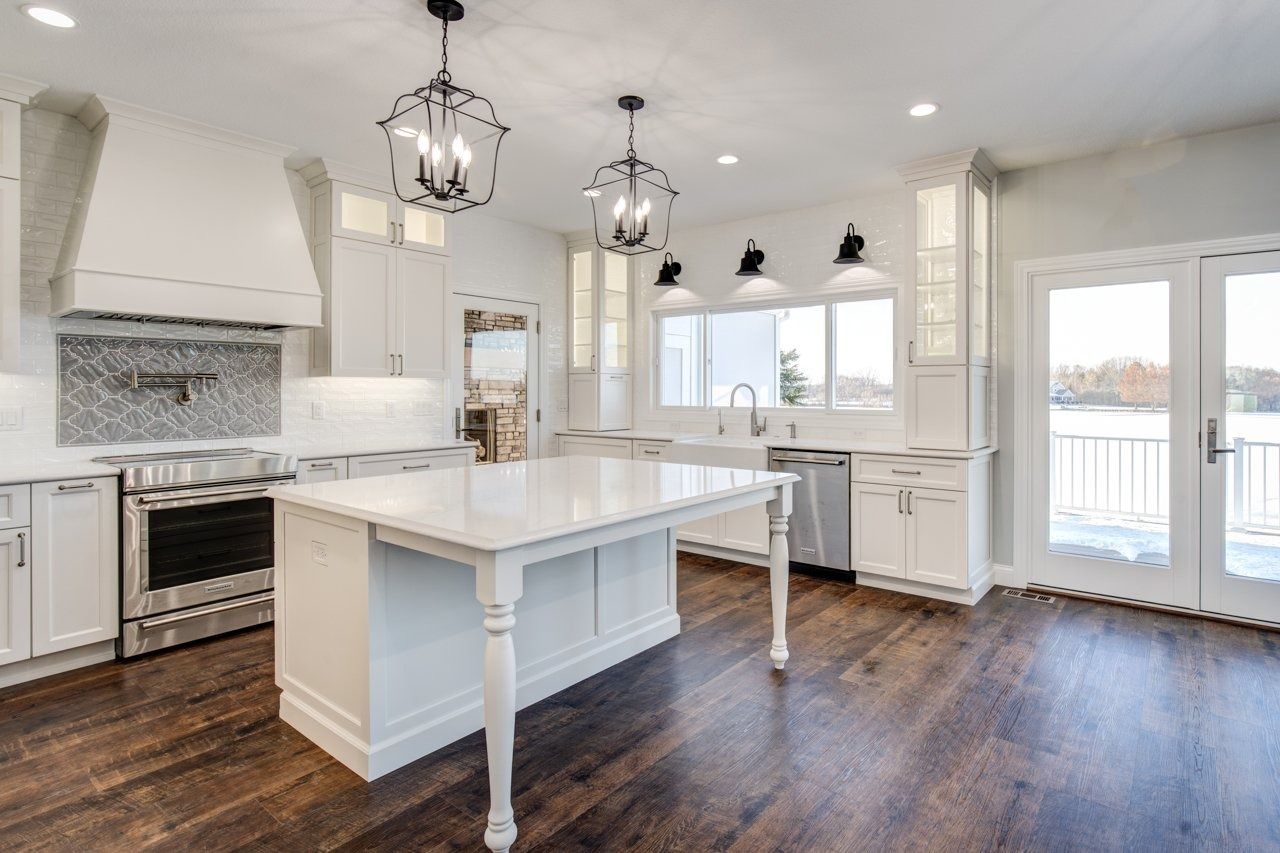 Bright white kitchen with a marble island, stainless steel appliances, and dark wood floors.