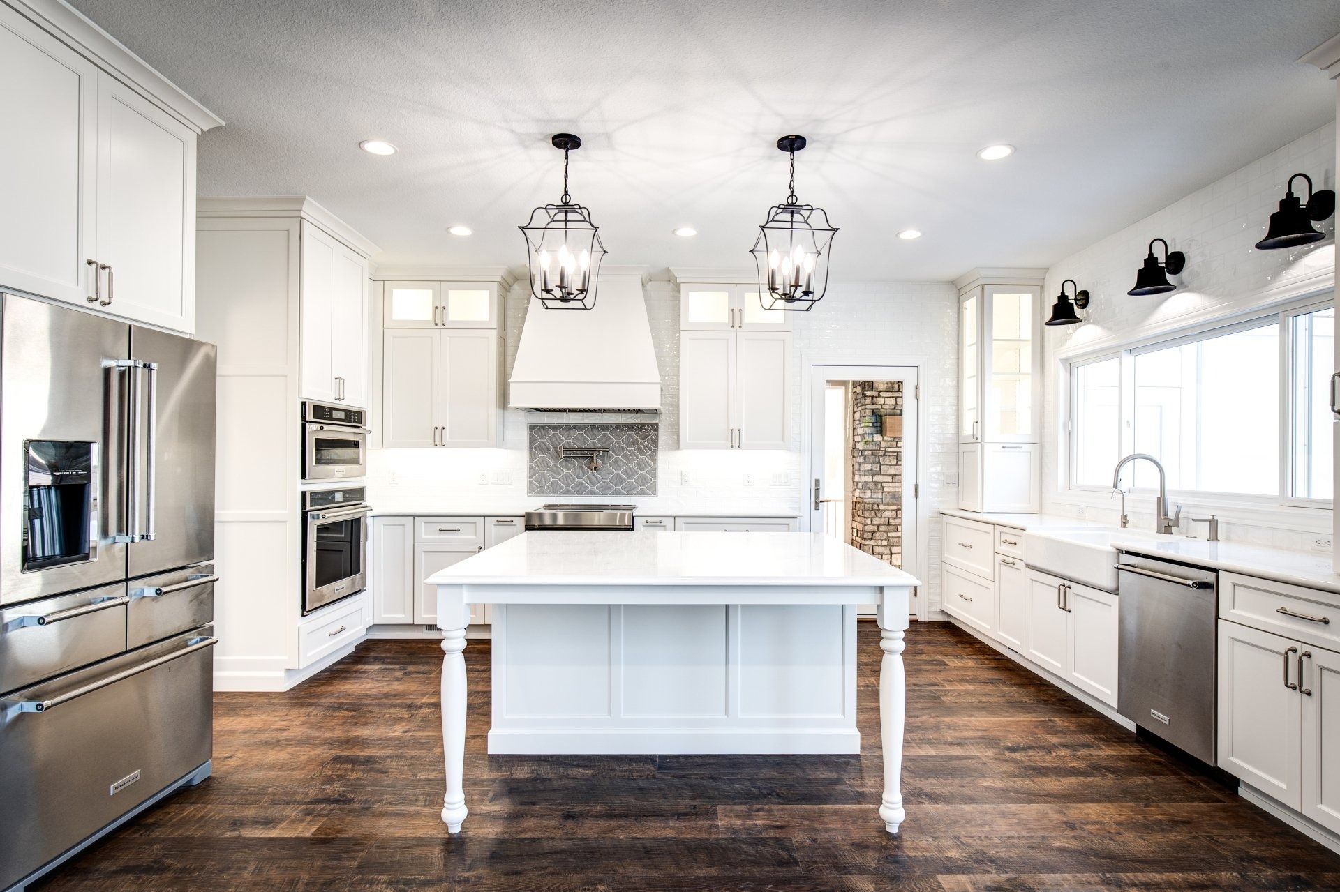 Modern white kitchen with stainless steel appliances, dark wood floors, and island.