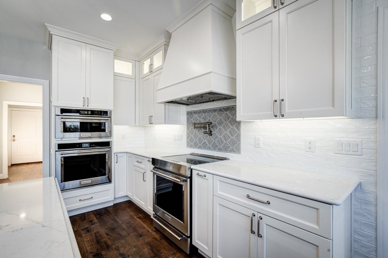 White kitchen with stainless steel appliances, white cabinets, and dark wood floor.