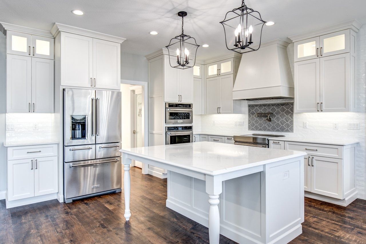 White kitchen with island, stainless steel appliances, dark wood floors, and pendant lights.