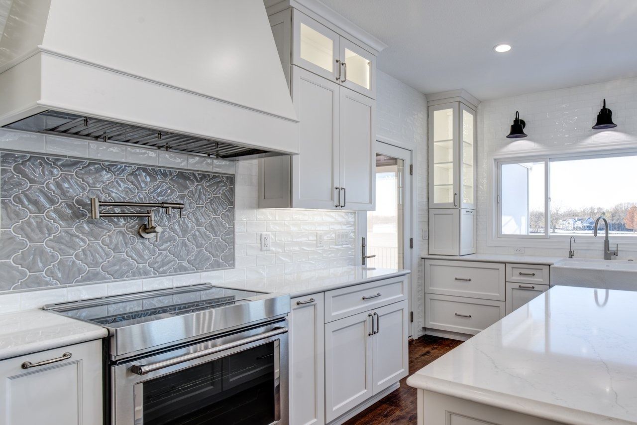 White kitchen with stainless steel appliances, white cabinets, and patterned gray backsplash.