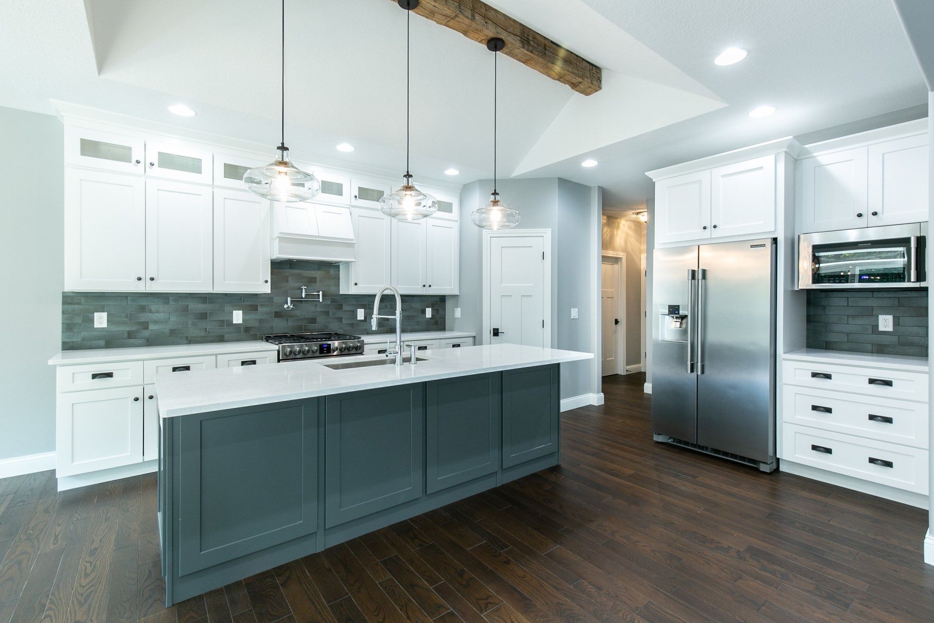 Modern kitchen with white cabinetry, teal island, stainless steel appliances, and dark wood floors.