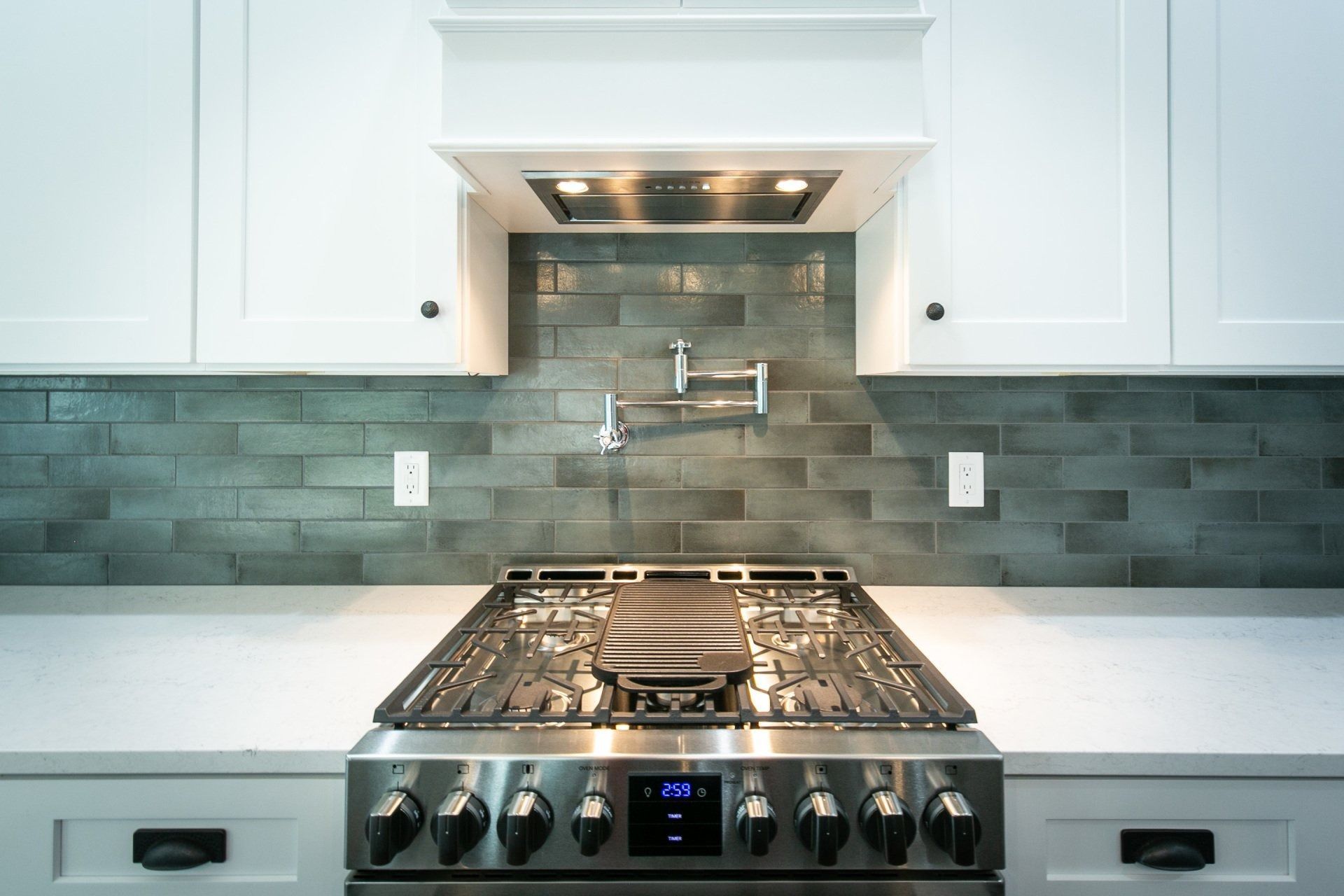 Stainless steel gas range in modern white kitchen with gray tile backsplash and pot filler.