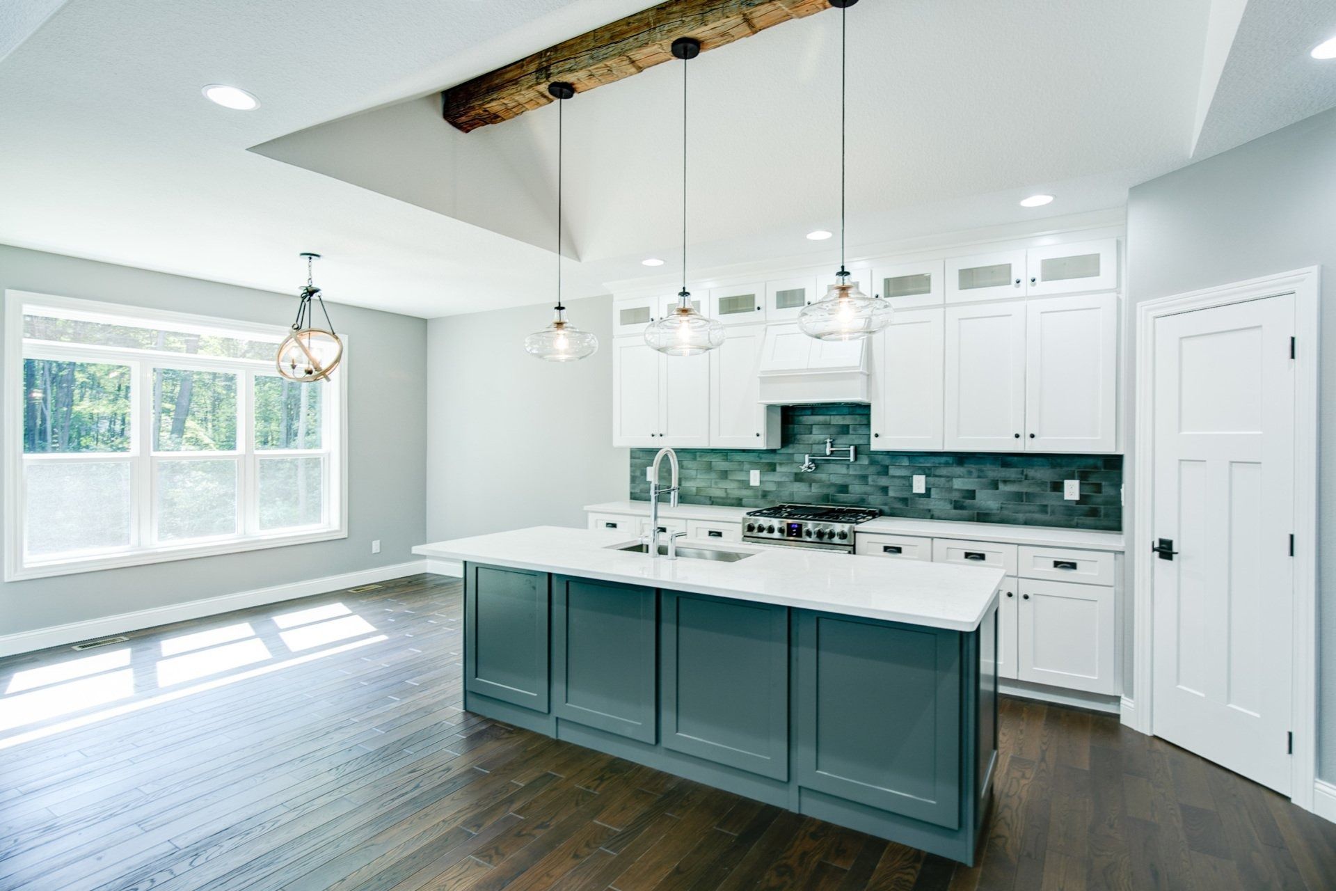 Modern kitchen with blue island, white cabinets, and wooden beam ceiling detail.